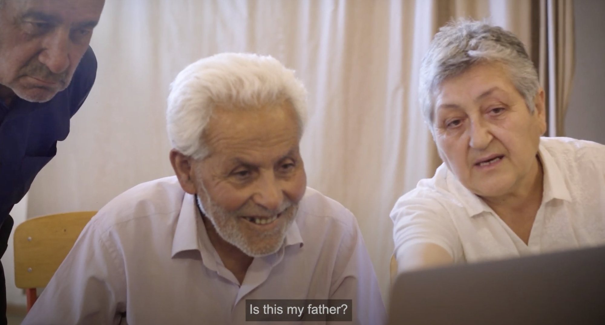 Two village elders lean in to look at scanned photographs on a laptop