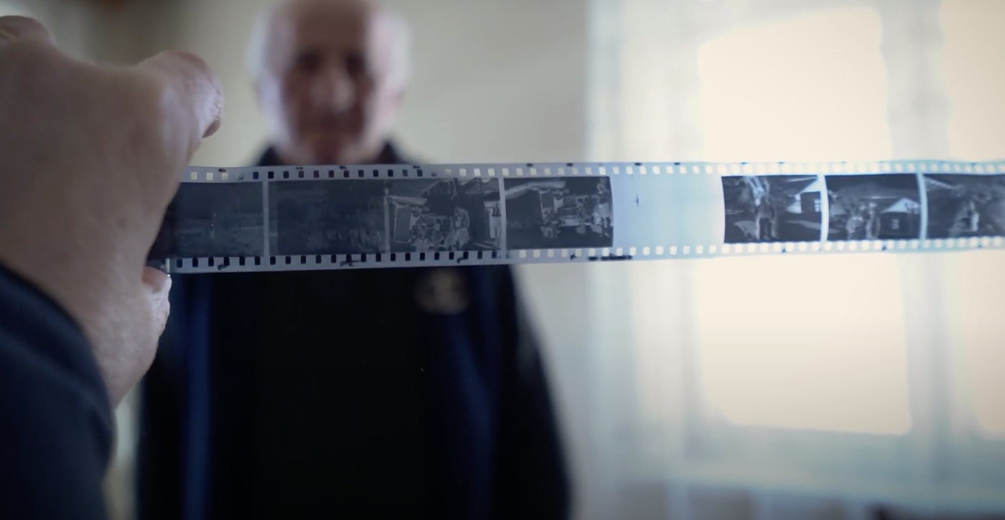 A hand holds a strip of old black and white negatives up to the light