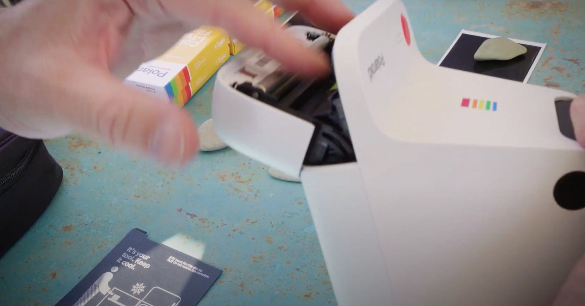 A hand lifts a Polaroid print from an instant camera