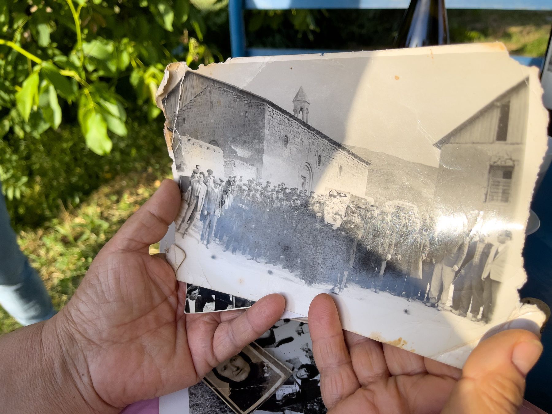 Two hands hold up an old black and white photograph of villagers