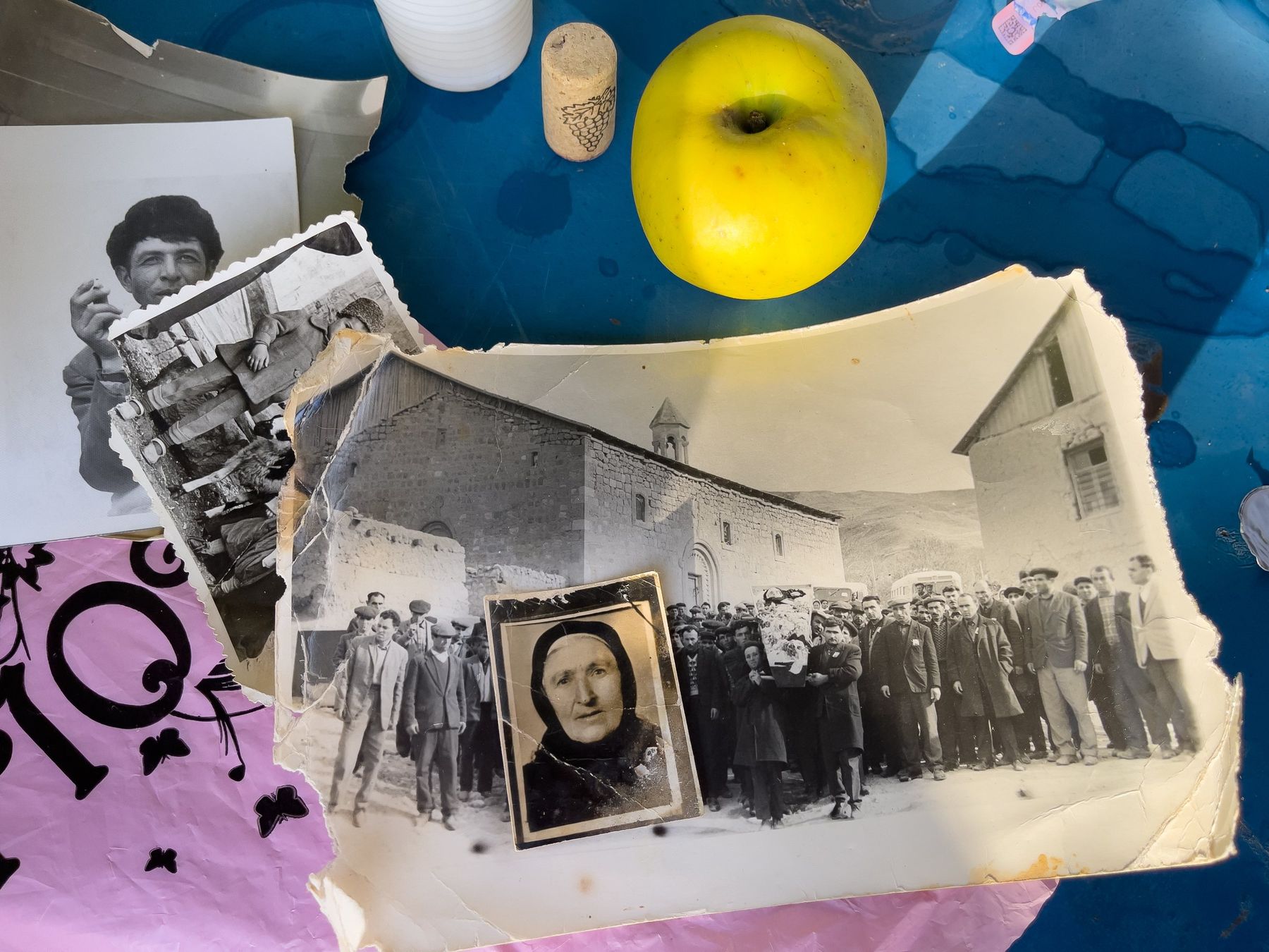 Old black and white photographs spread on a table, beside an apple