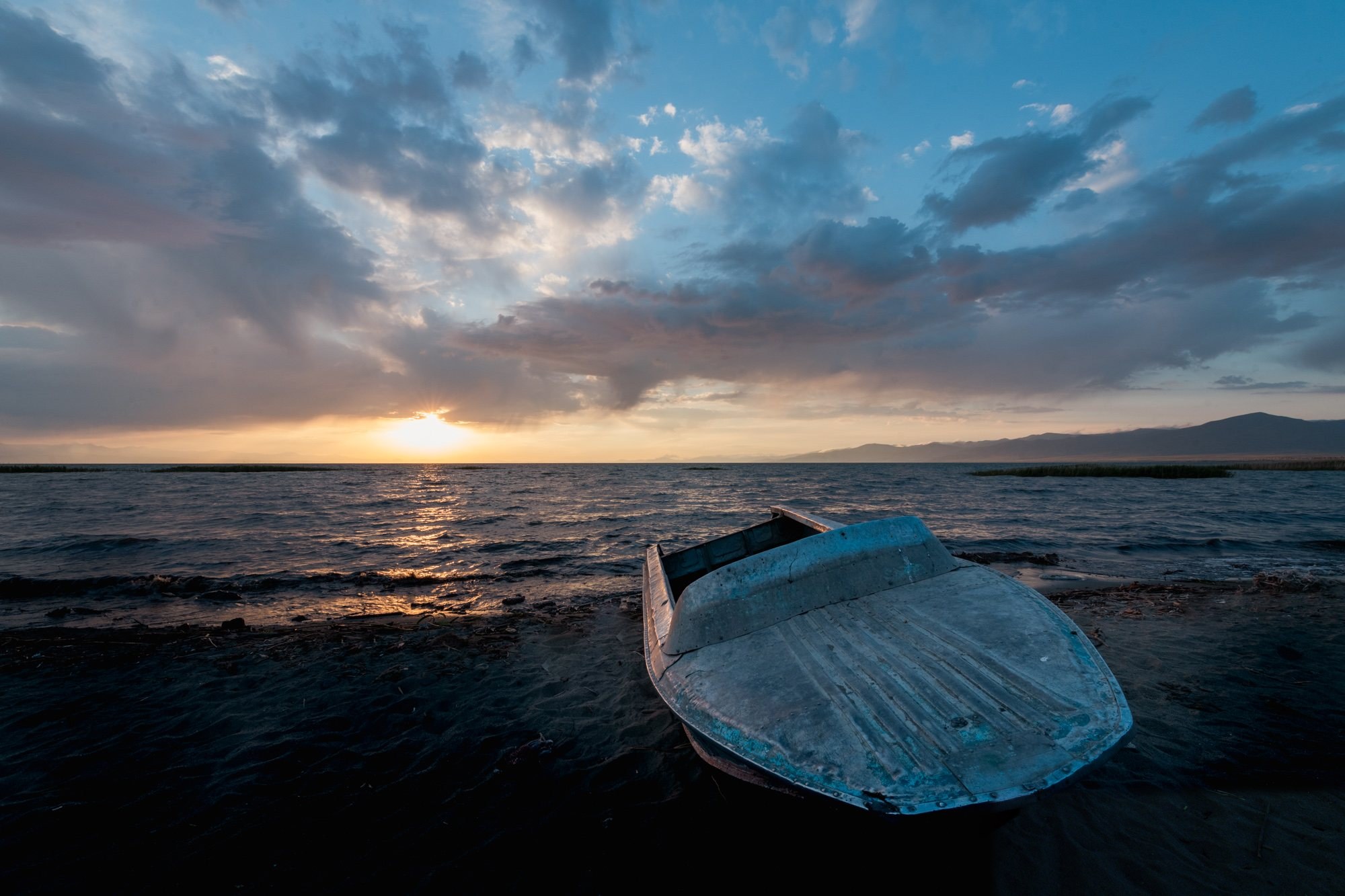 A small metal boat pulled up on a dark shore at sunset