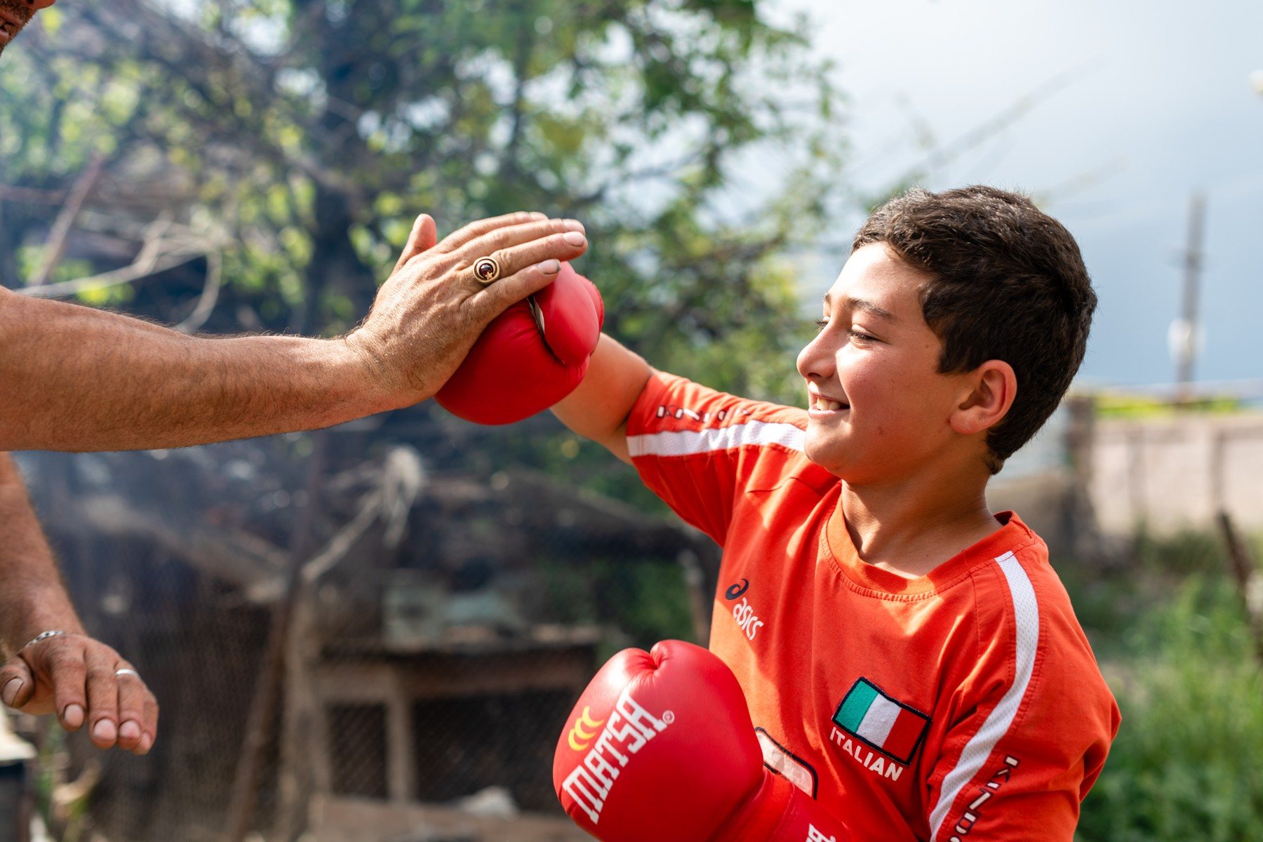 A smiling boy in red gloves punches into a man’s open palm