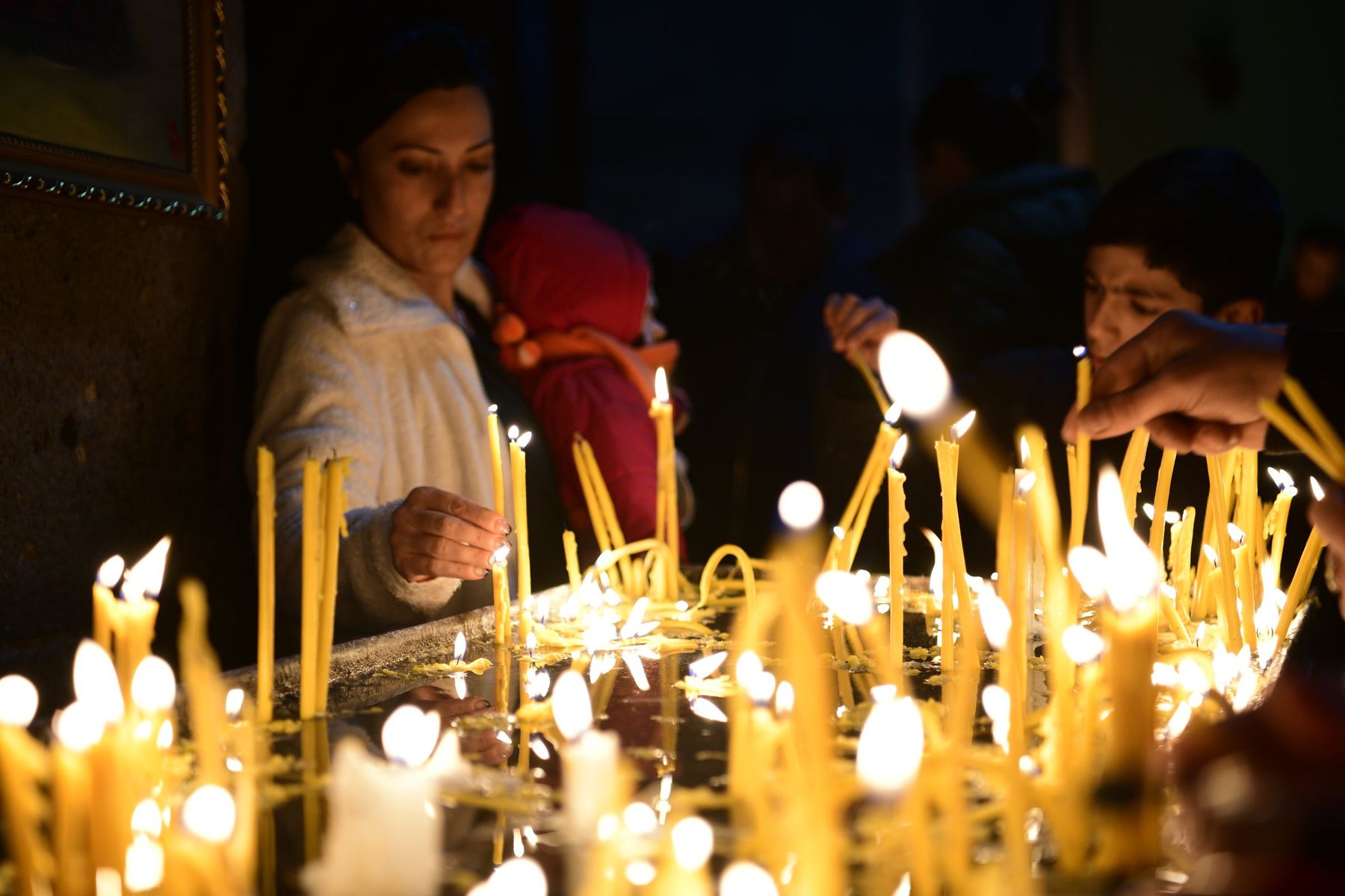 Children light thin candles in a dark church