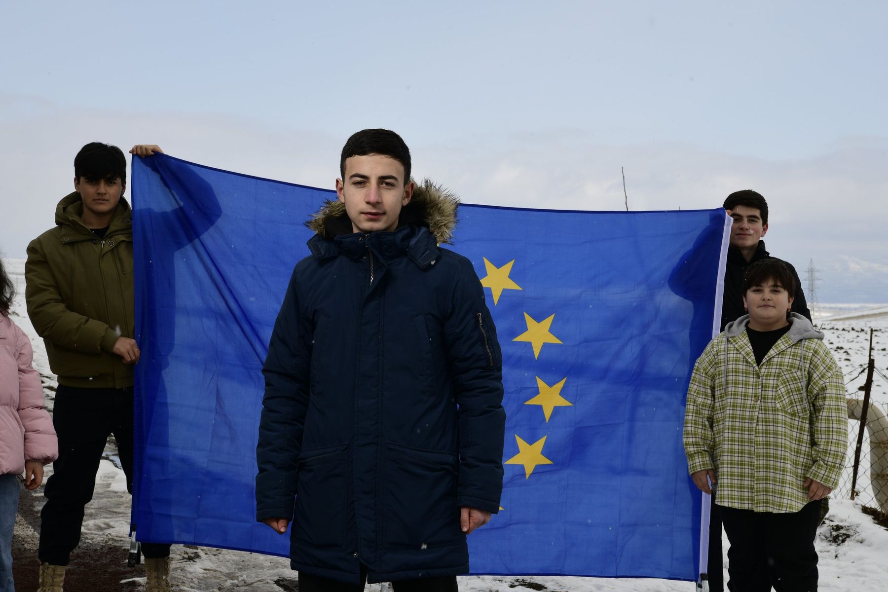 A teenage boy stands before a European Union flag held by friends
