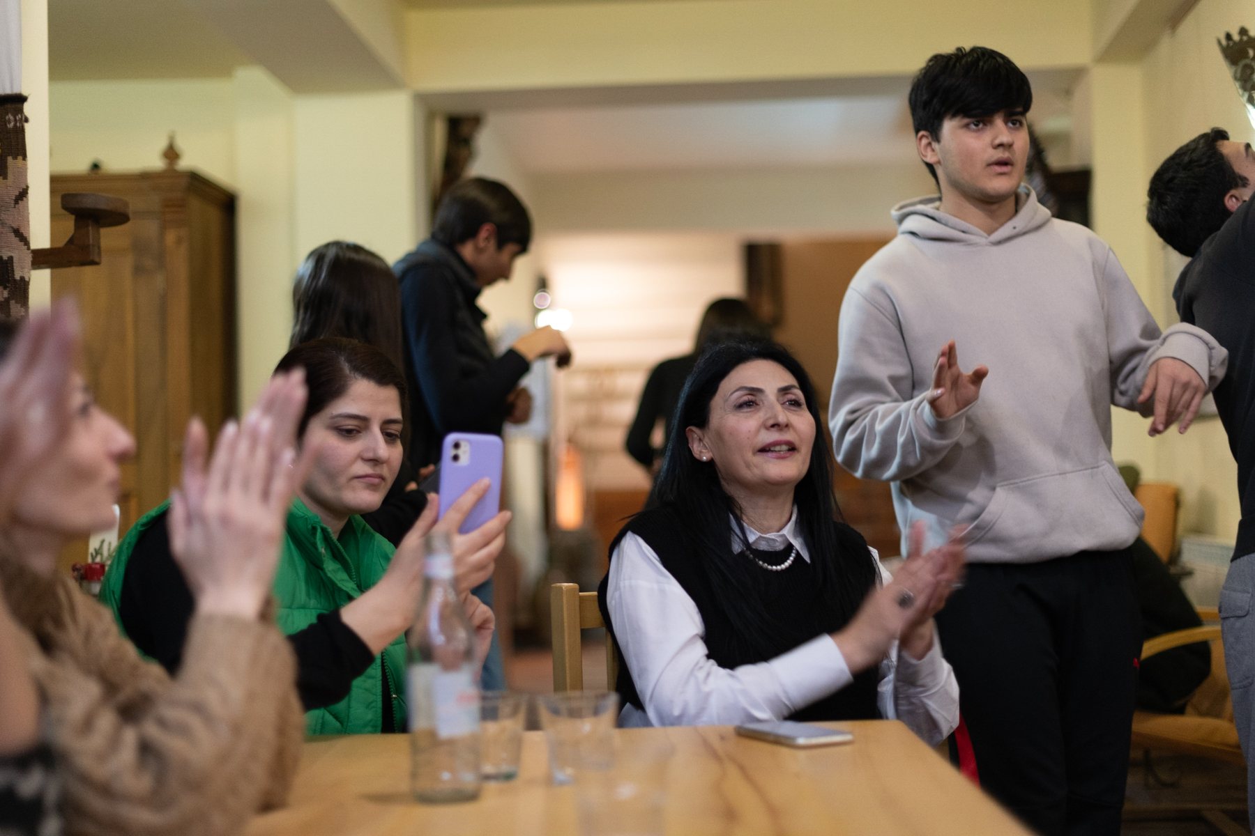 Women and teenagers laugh and clap around a dinner table