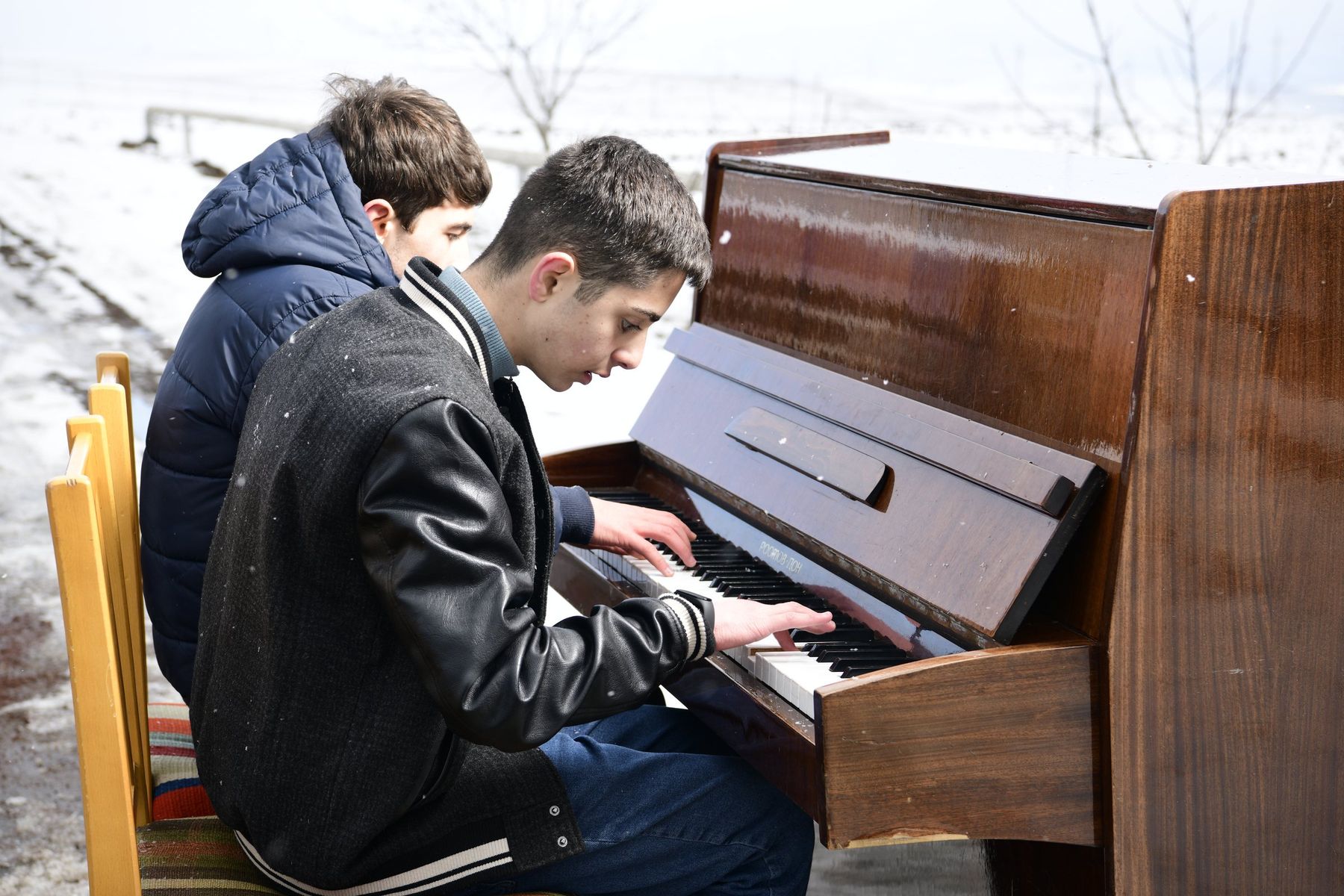 A boy in a leather jacket plays piano outdoors
