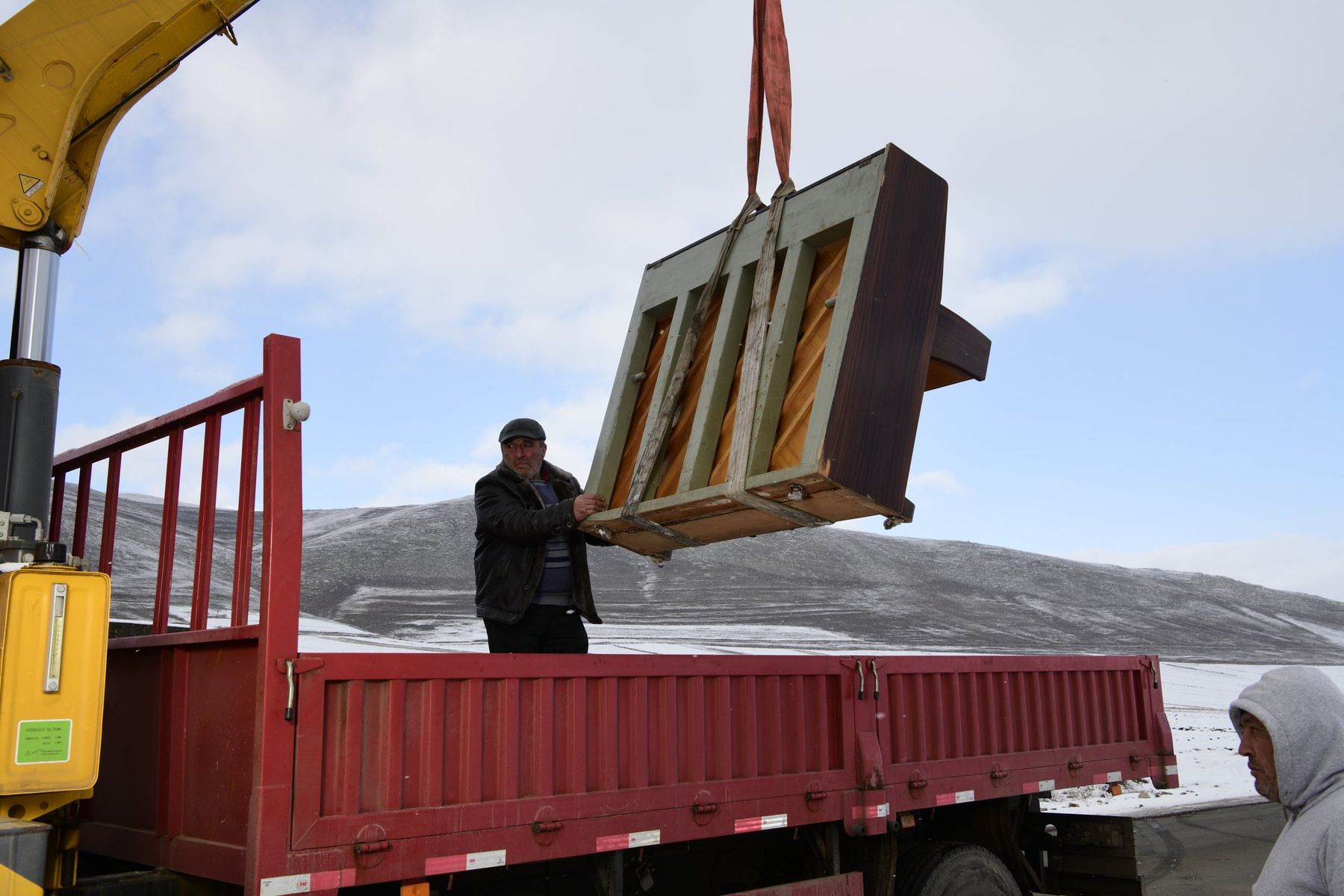 A crane lifts a wooden piano off a red truck