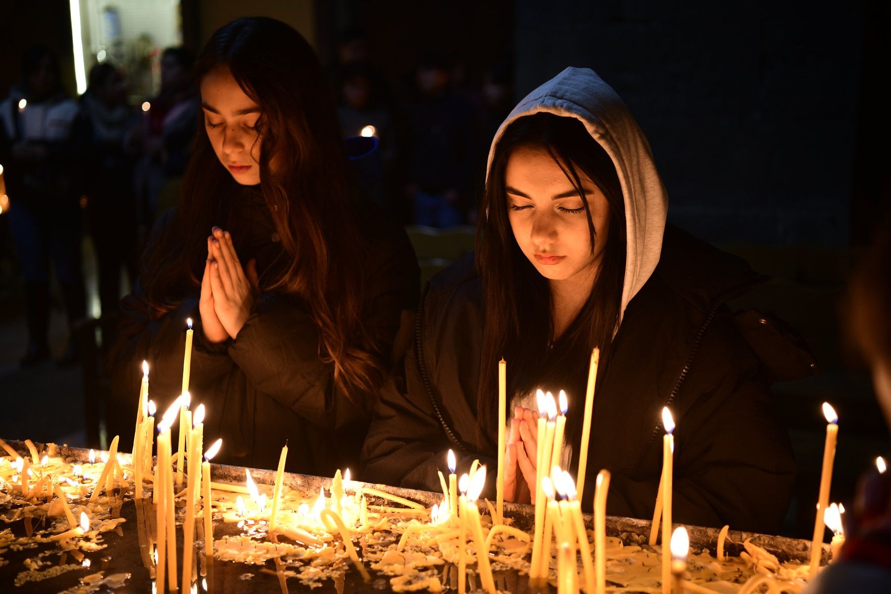 Two girls pray over a tray of burning candles