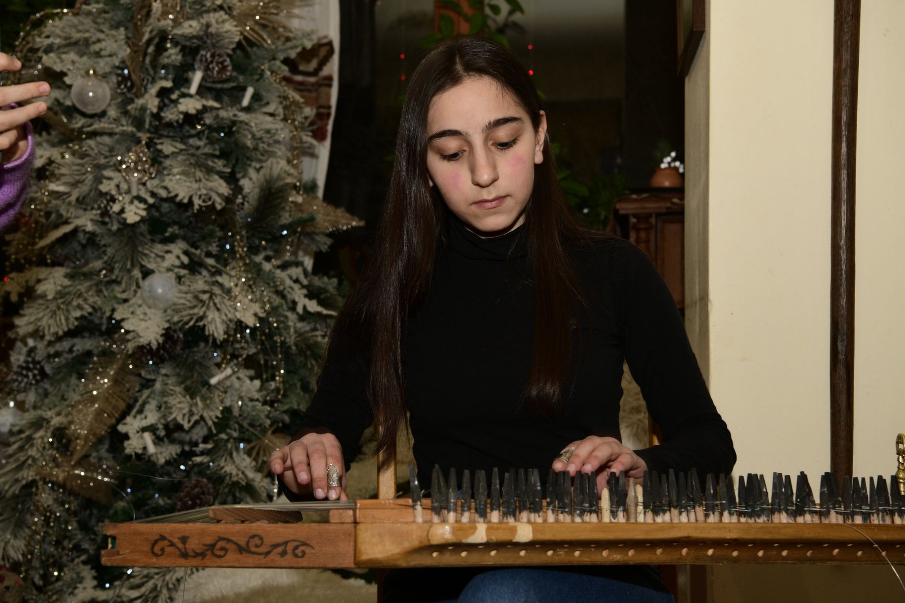 A girl plays the qanun beside a Christmas tree