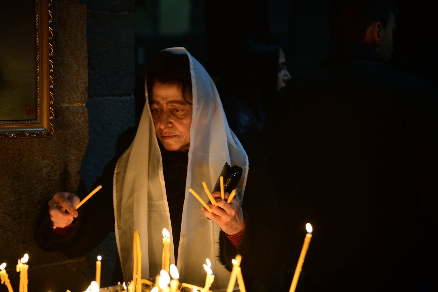 A woman in a white shawl lights a candle