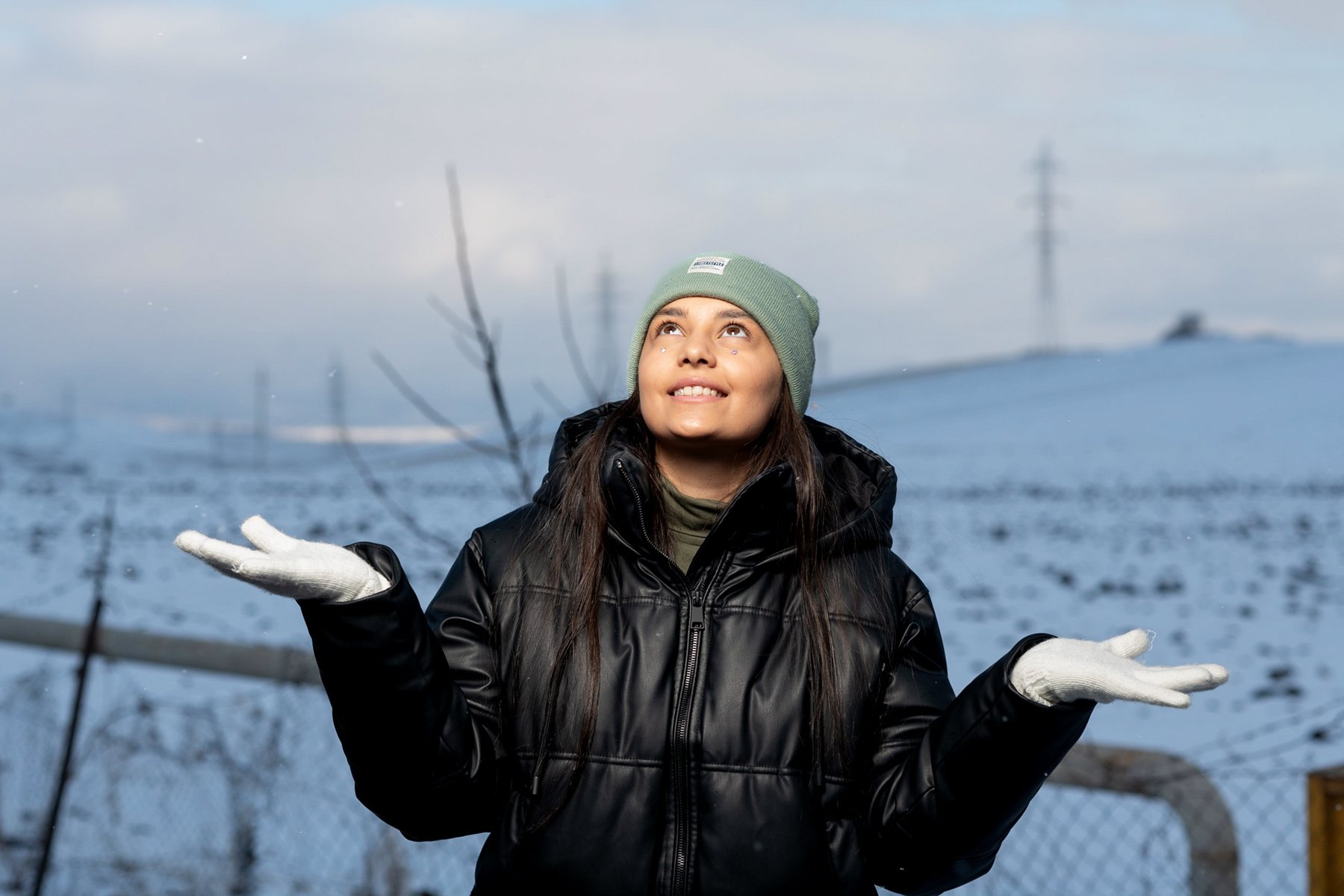 A girl in a black coat looks up into falling snow