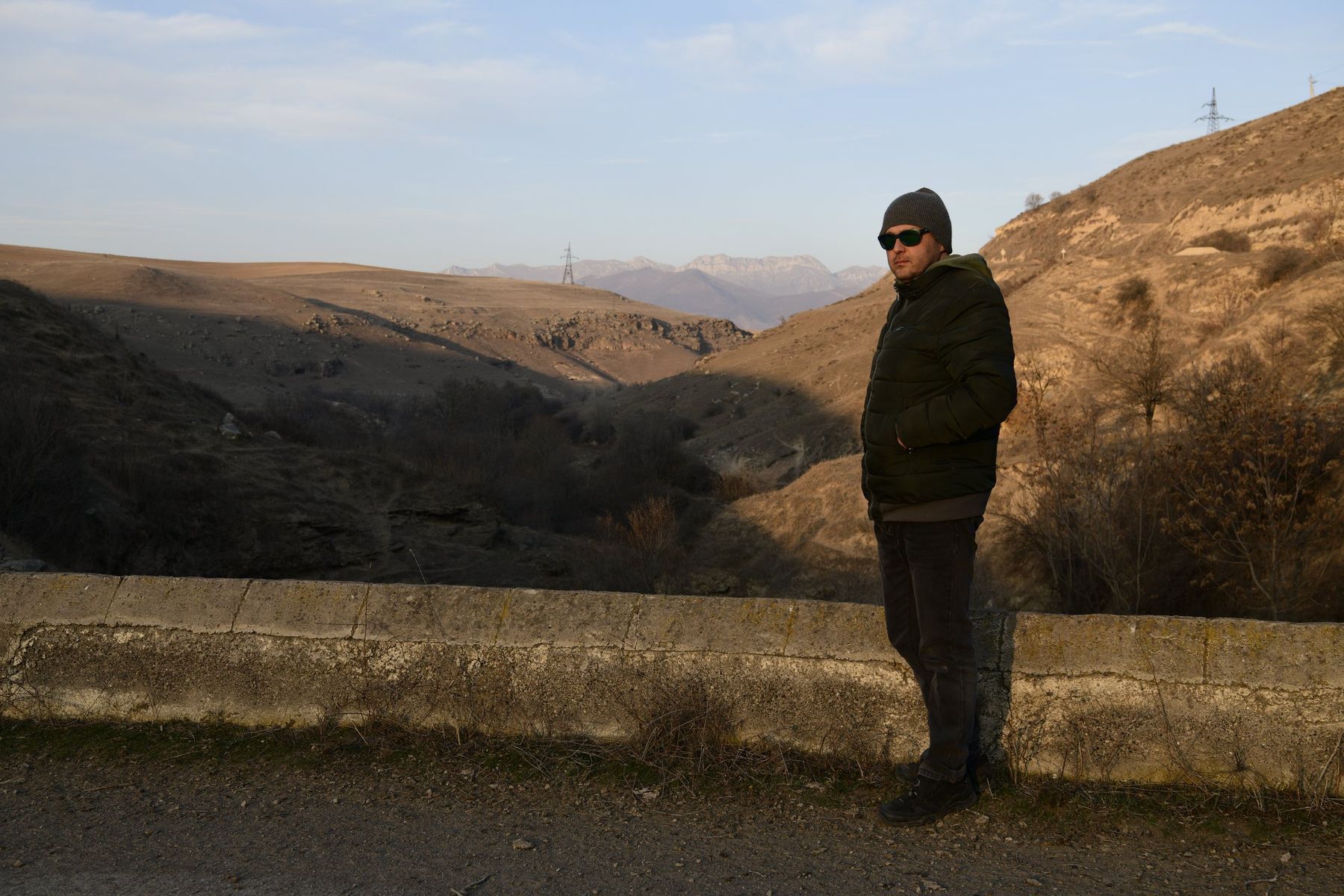 A man stands by a roadside wall above a wide valley