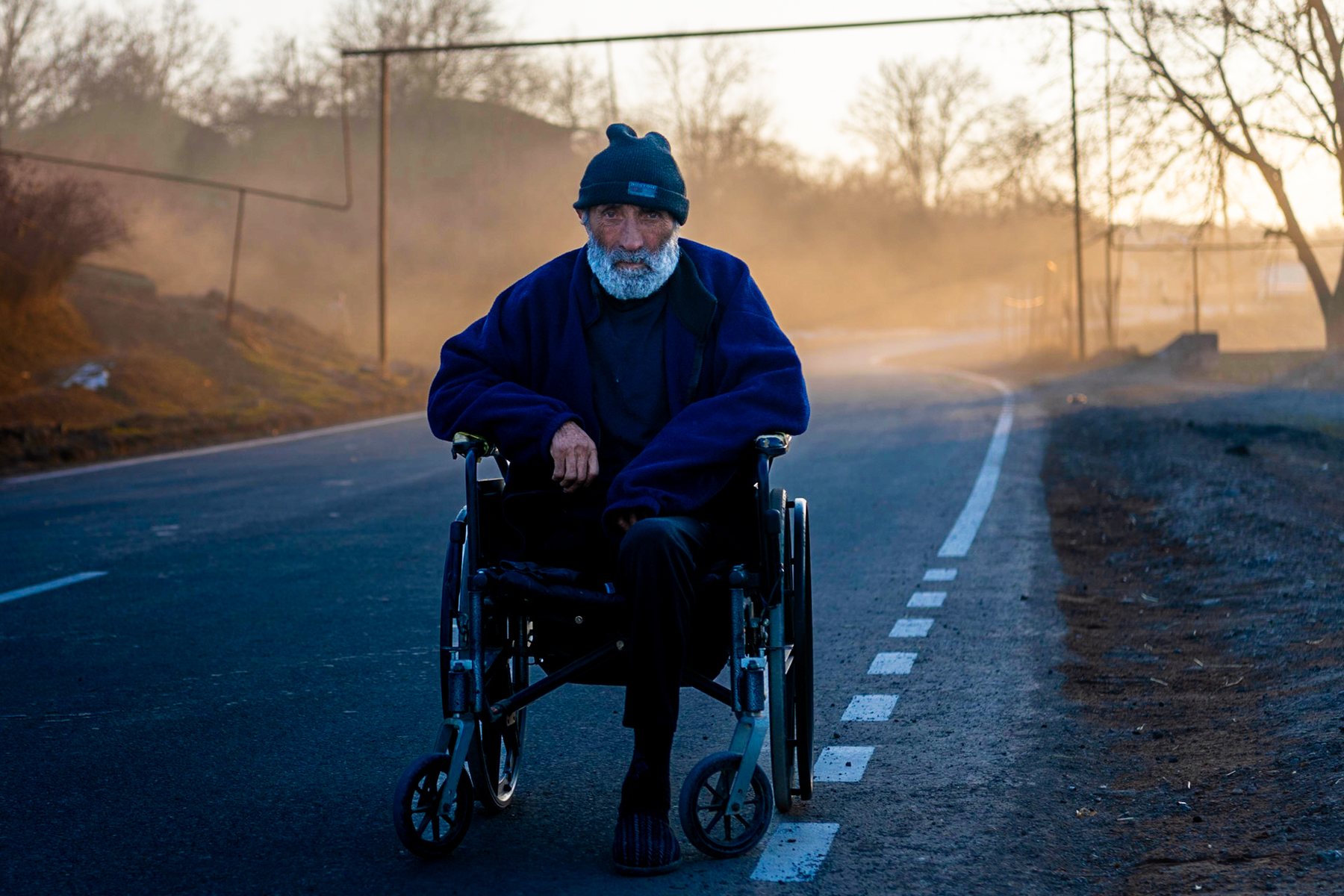 A man in a wheelchair on an empty road, mist behind him