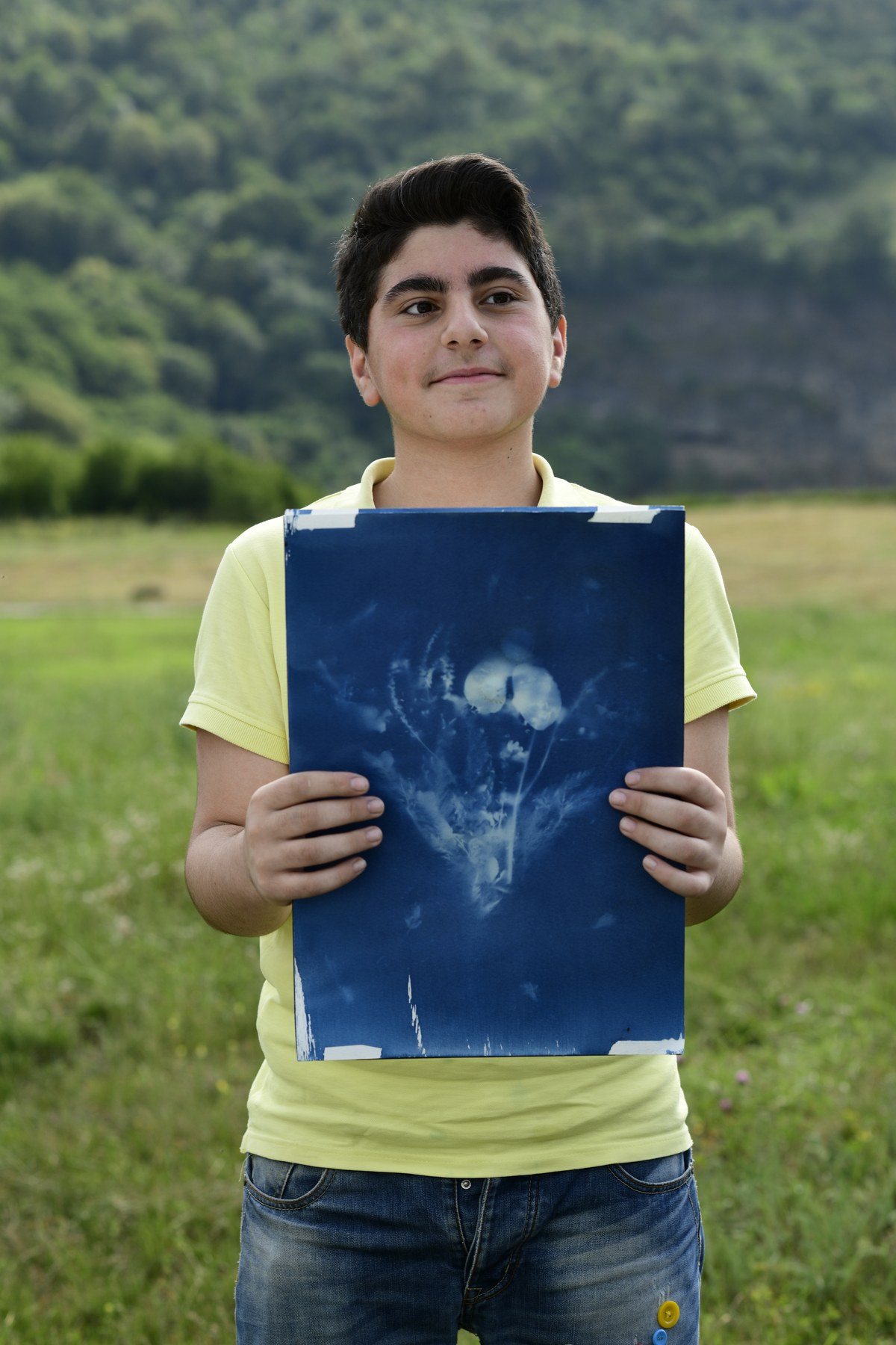 A boy in a yellow T-shirt holds up a blue print of a flower