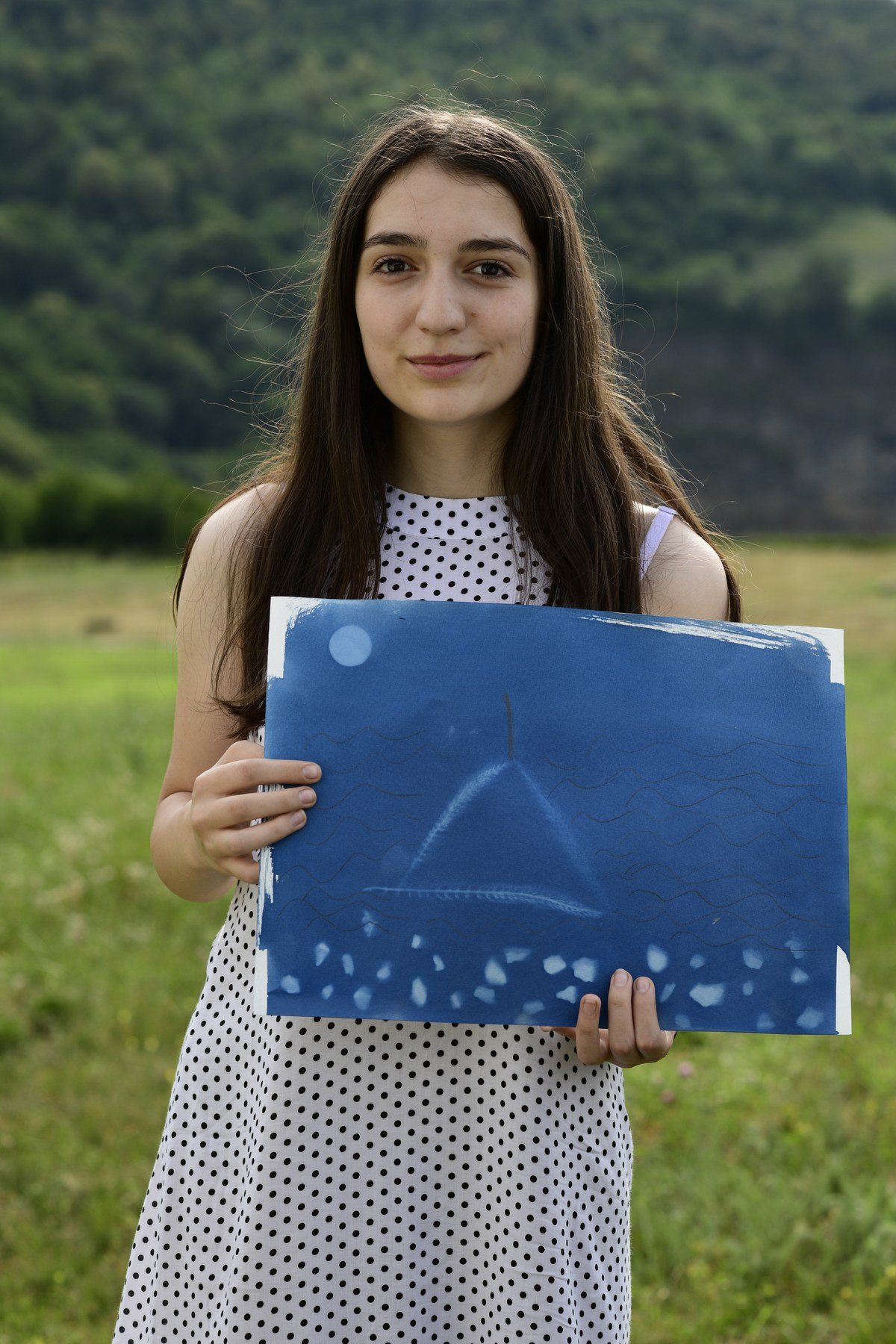 A girl in a spotted dress holds a blue print with a triangle shape