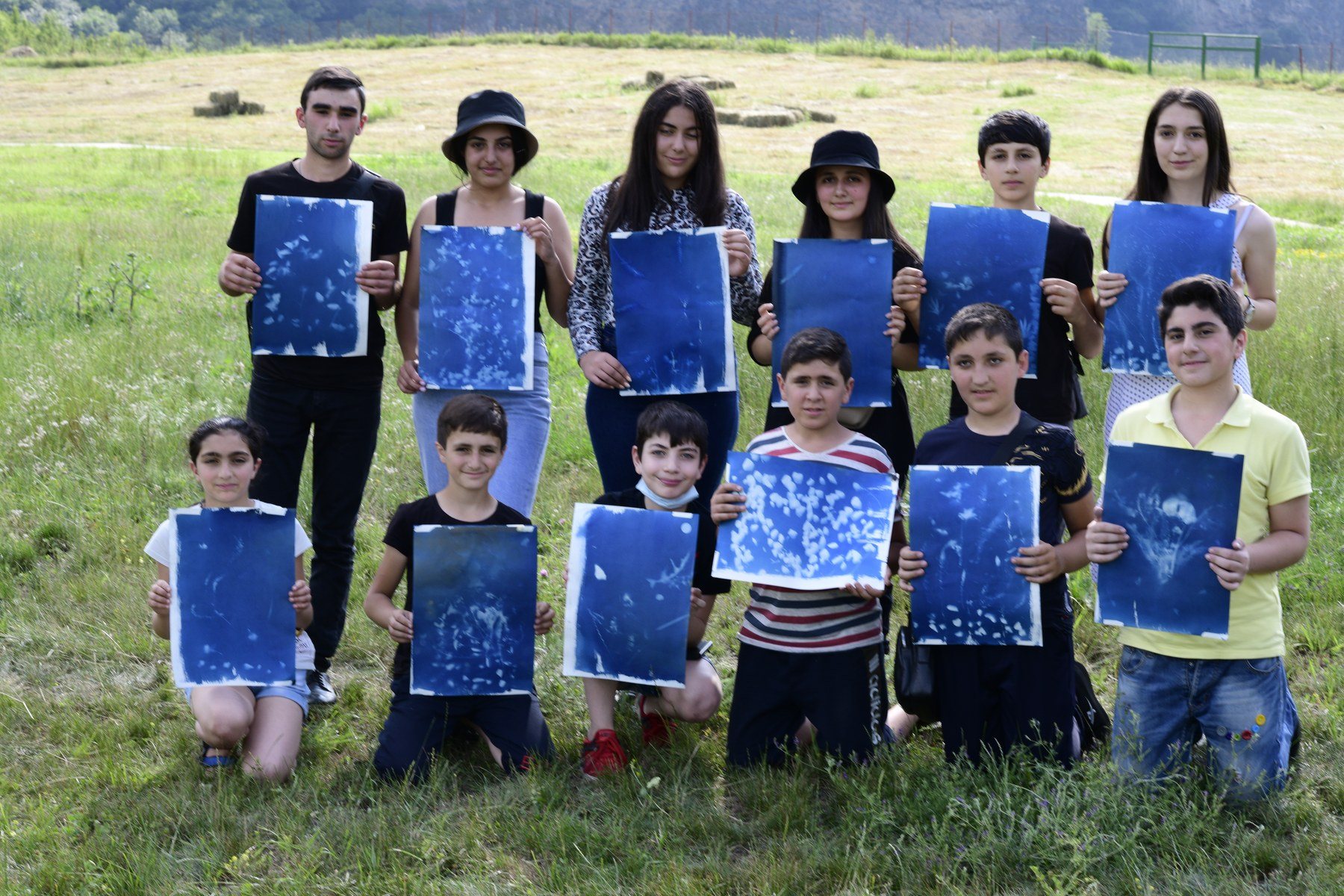 A group of teenagers stand in a field, each holding up a blue cyanotype print