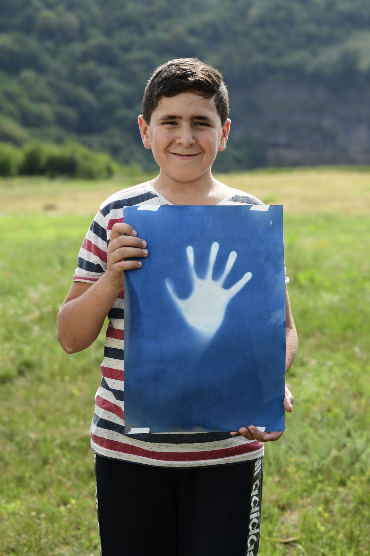 A boy in a striped shirt holds up a blue print of a hand