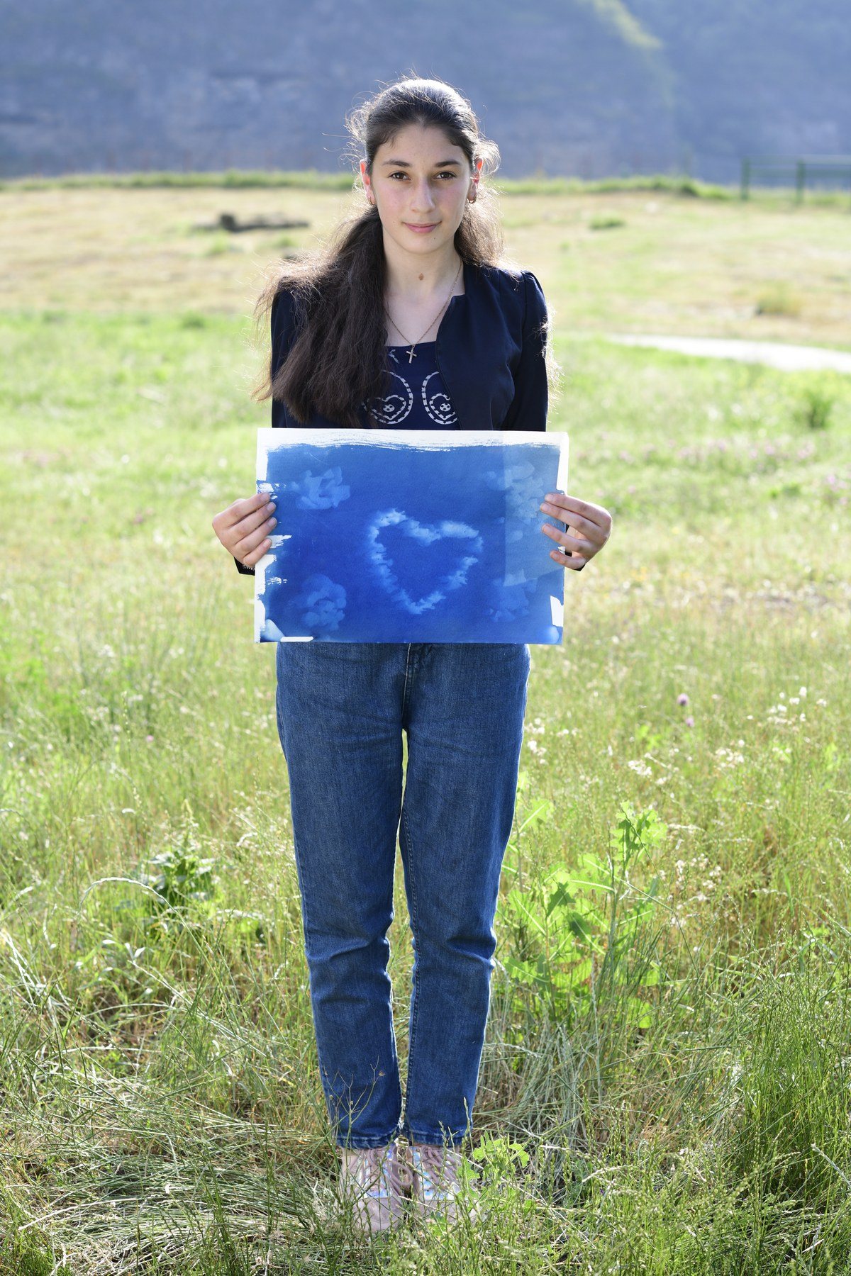 A girl in a dark jacket holds a blue print of a heart