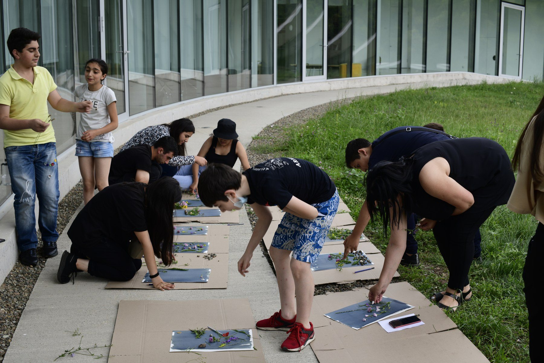 Teenagers kneel along a path, laying out sheets of paper in the sun