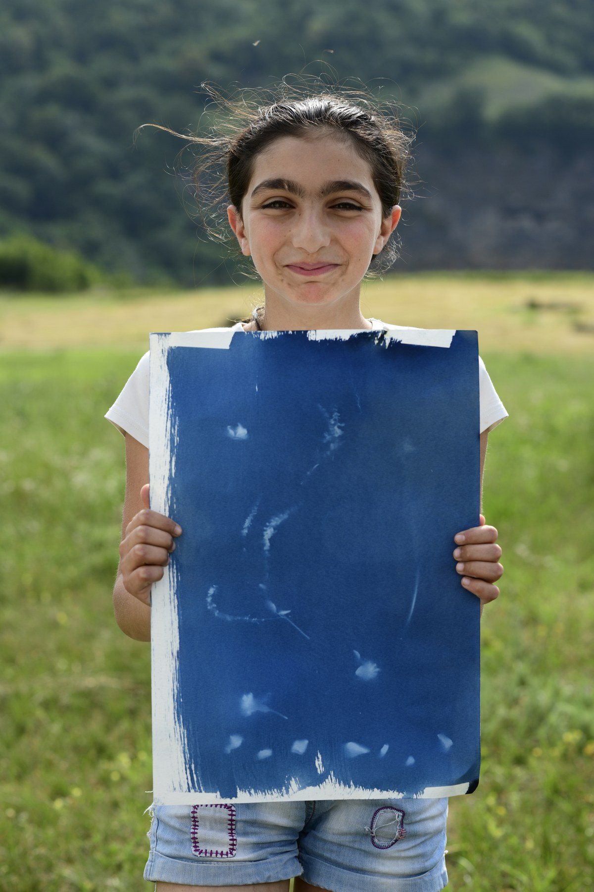 A smiling girl holds a large blue print in front of her