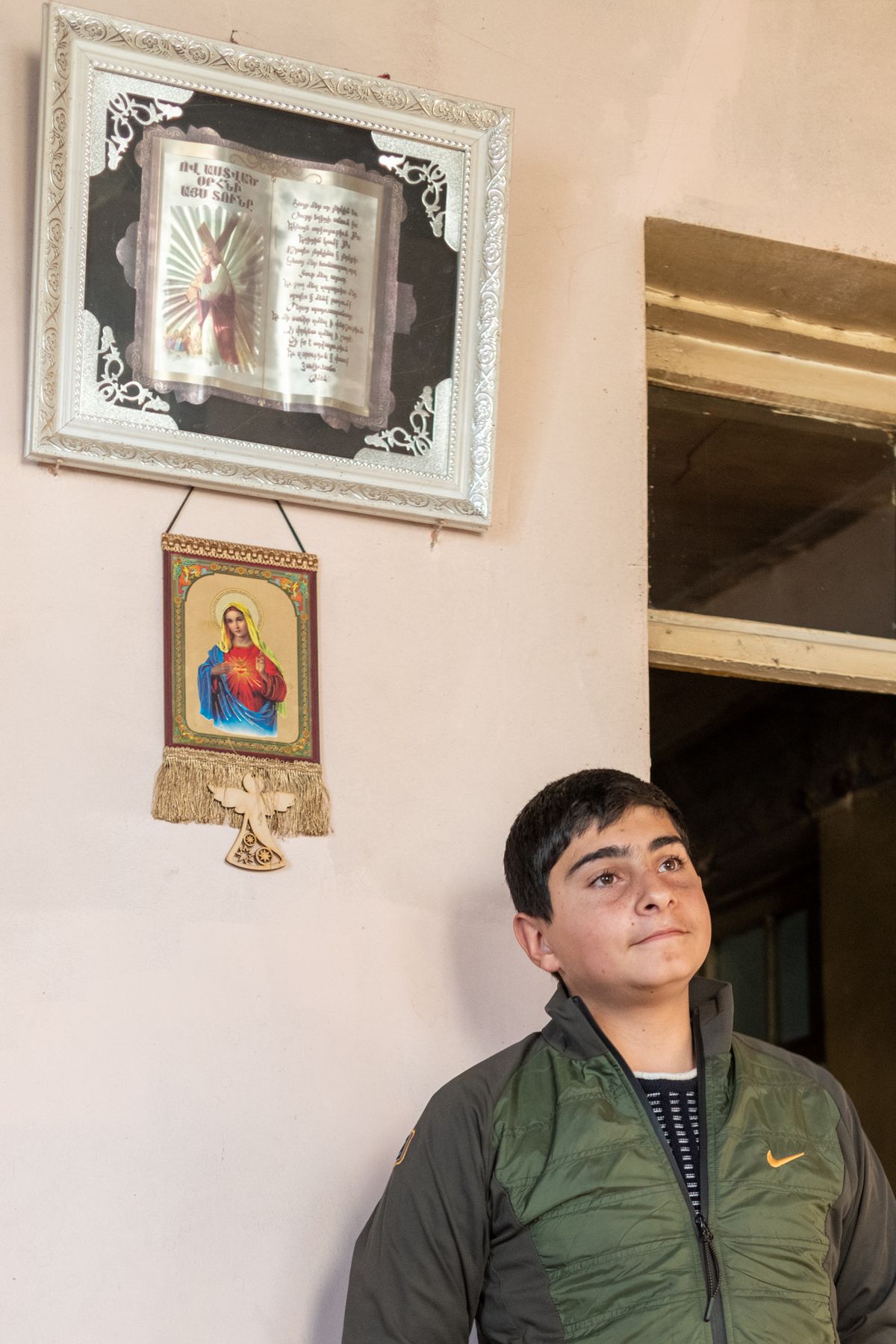 A boy stands beneath an icon and a framed photograph