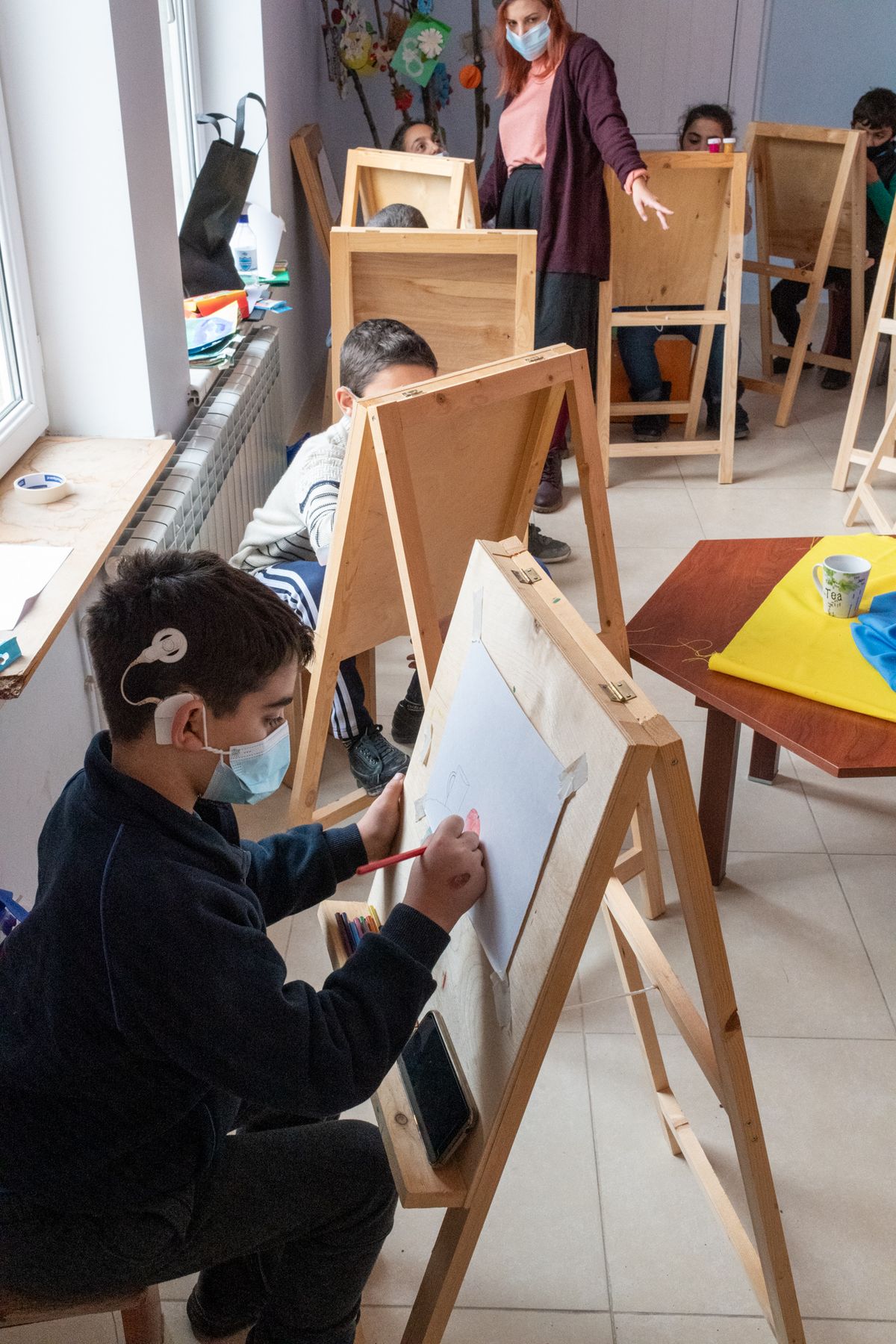 A masked child paints at an easel
