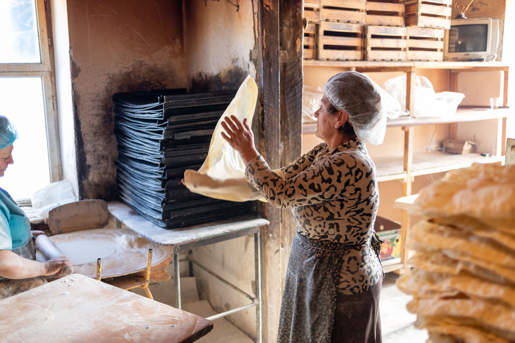 A woman lifts a sheet of lavash in a small bakery