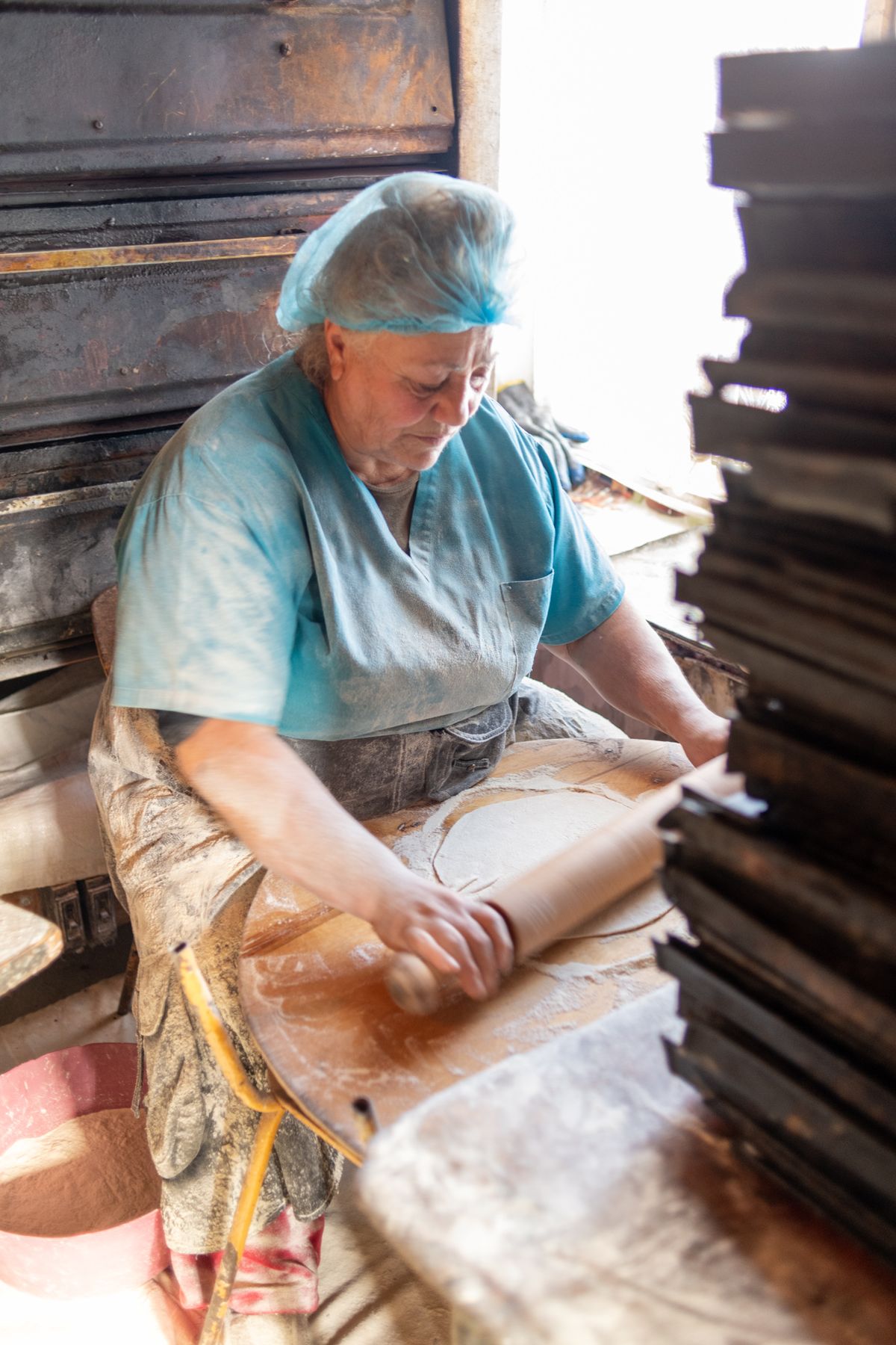 A baker in a hairnet rolls out lavash dough