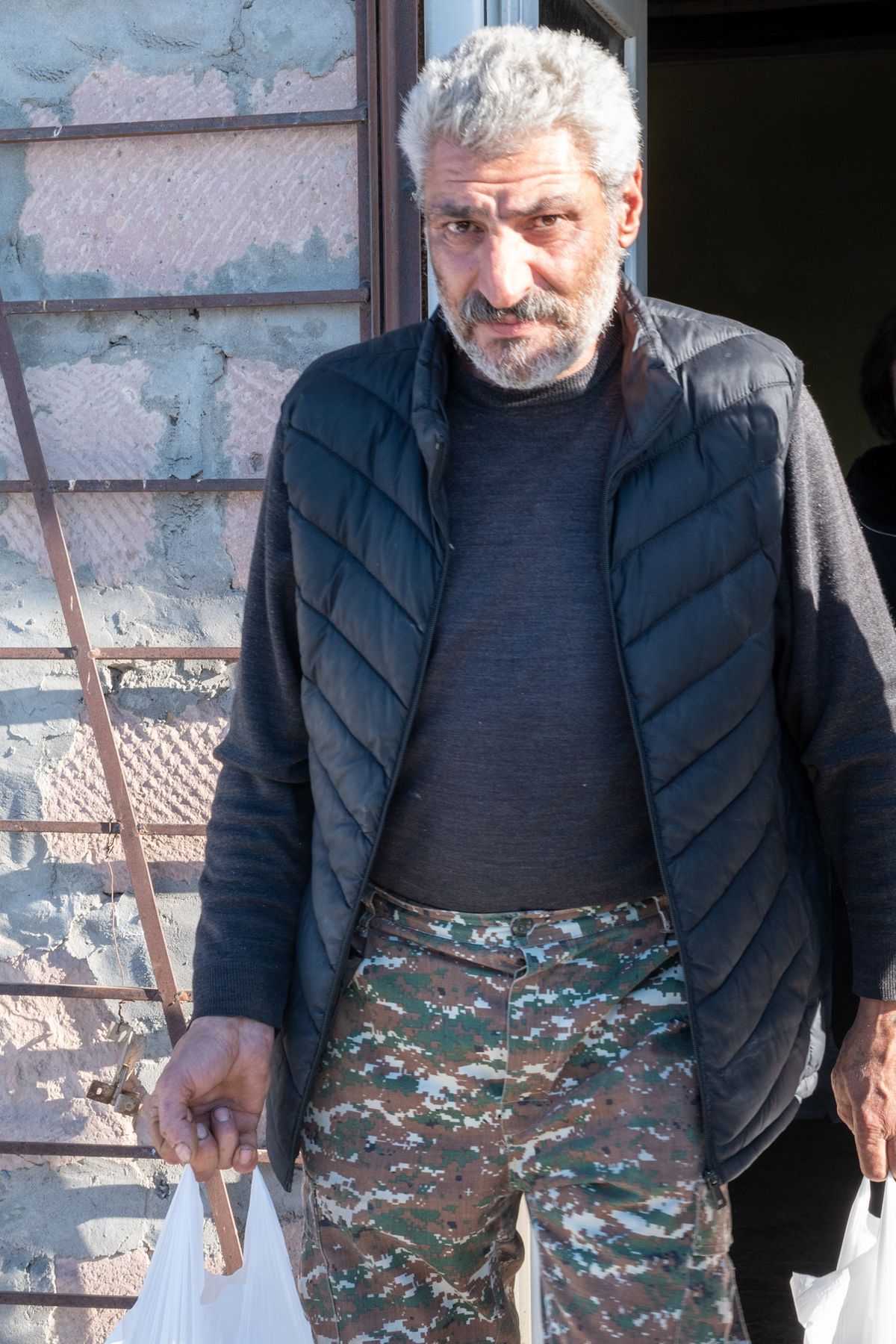 A grey-haired man in camouflage trousers carries a bag