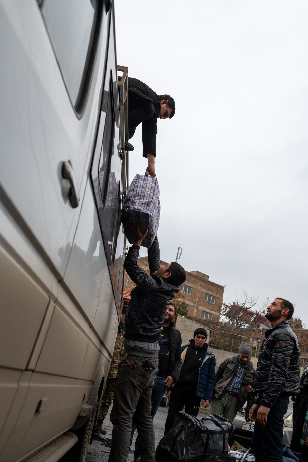 A man on a minibus roof hands down a bag