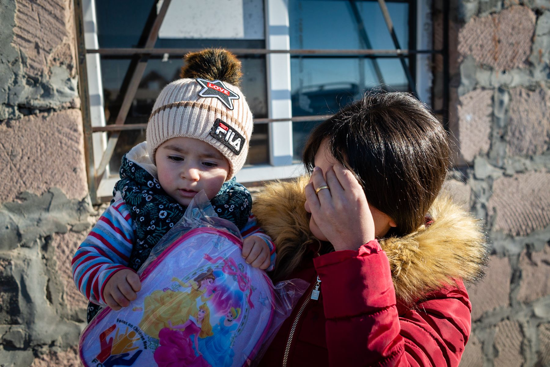 A woman holds a small child in a bright knitted hat