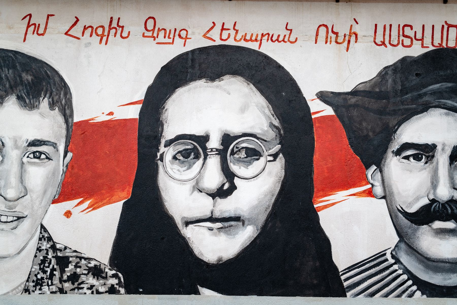 A painted mural of three faces under Armenian lettering