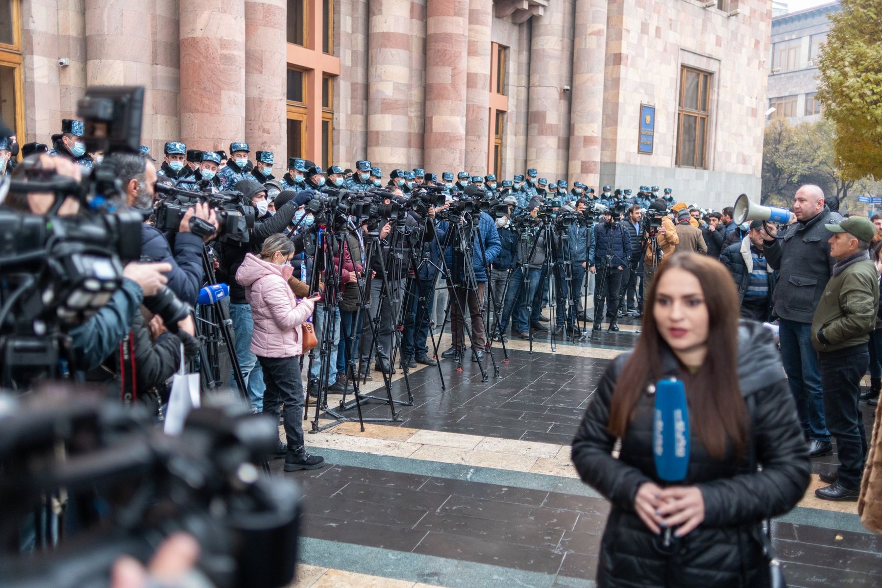 A reporter speaks to camera in front of a line of police and press