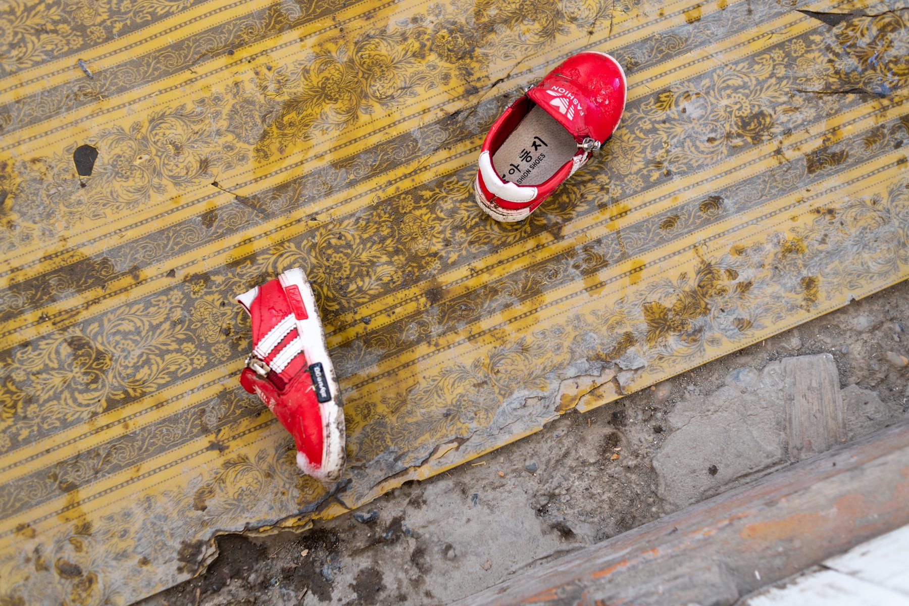 A pair of small red children’s shoes on a worn patterned floor