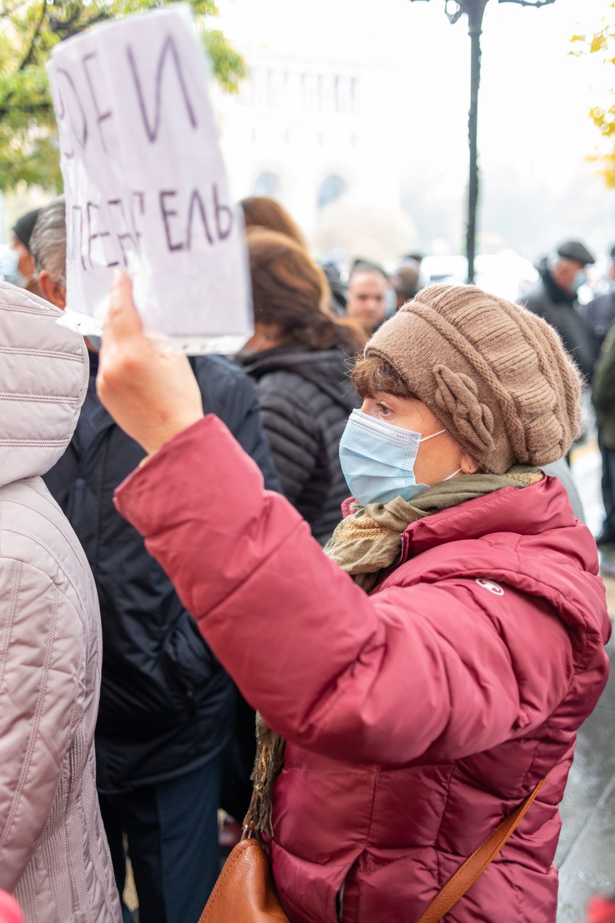A woman in a mask holds up a handwritten sign