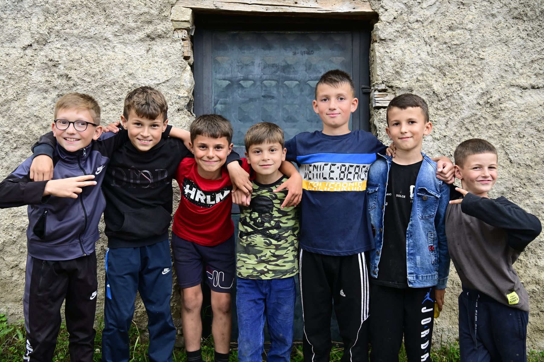 A group of boys pose in a line in front of a stone wall