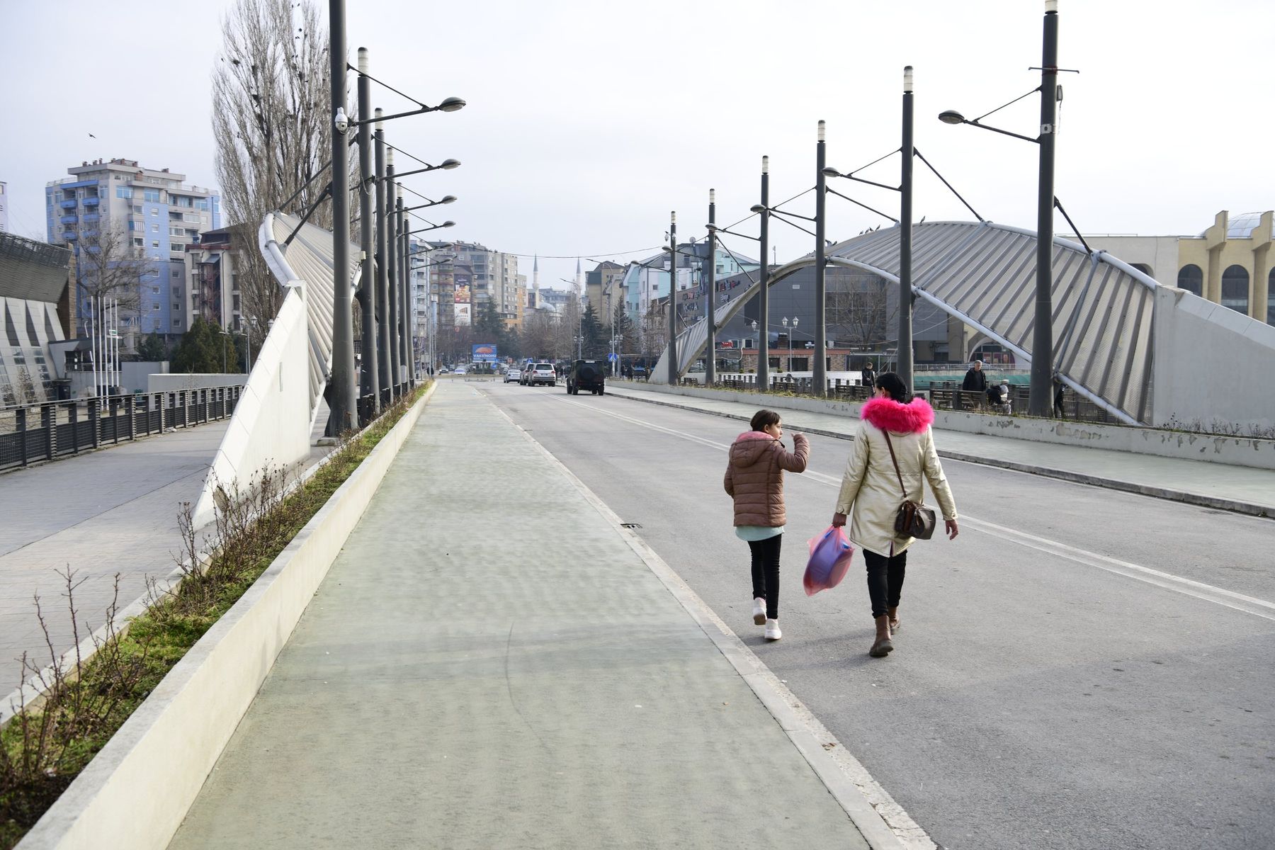 Two women walk across a wide, empty bridge