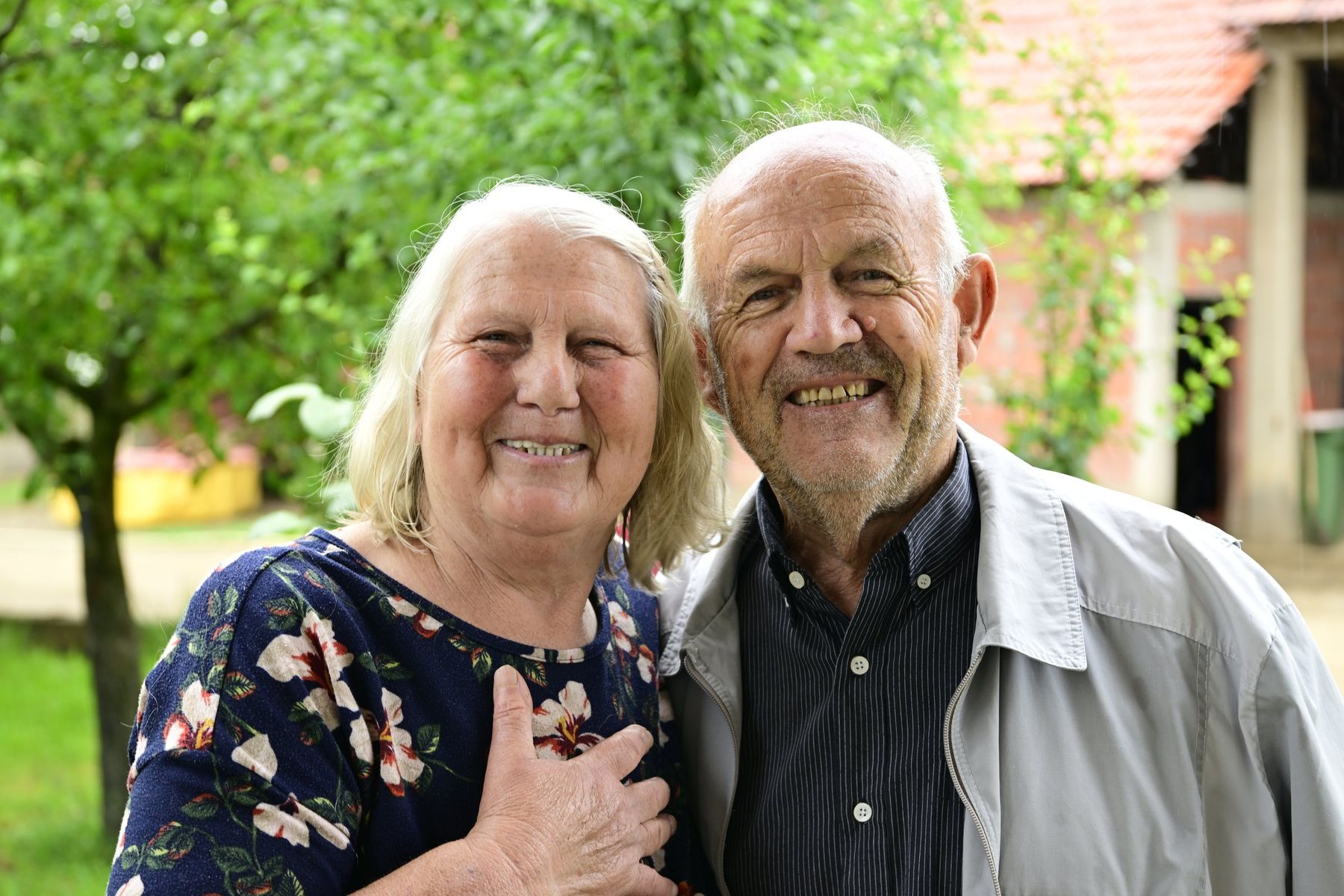 An elderly couple smile together in a garden