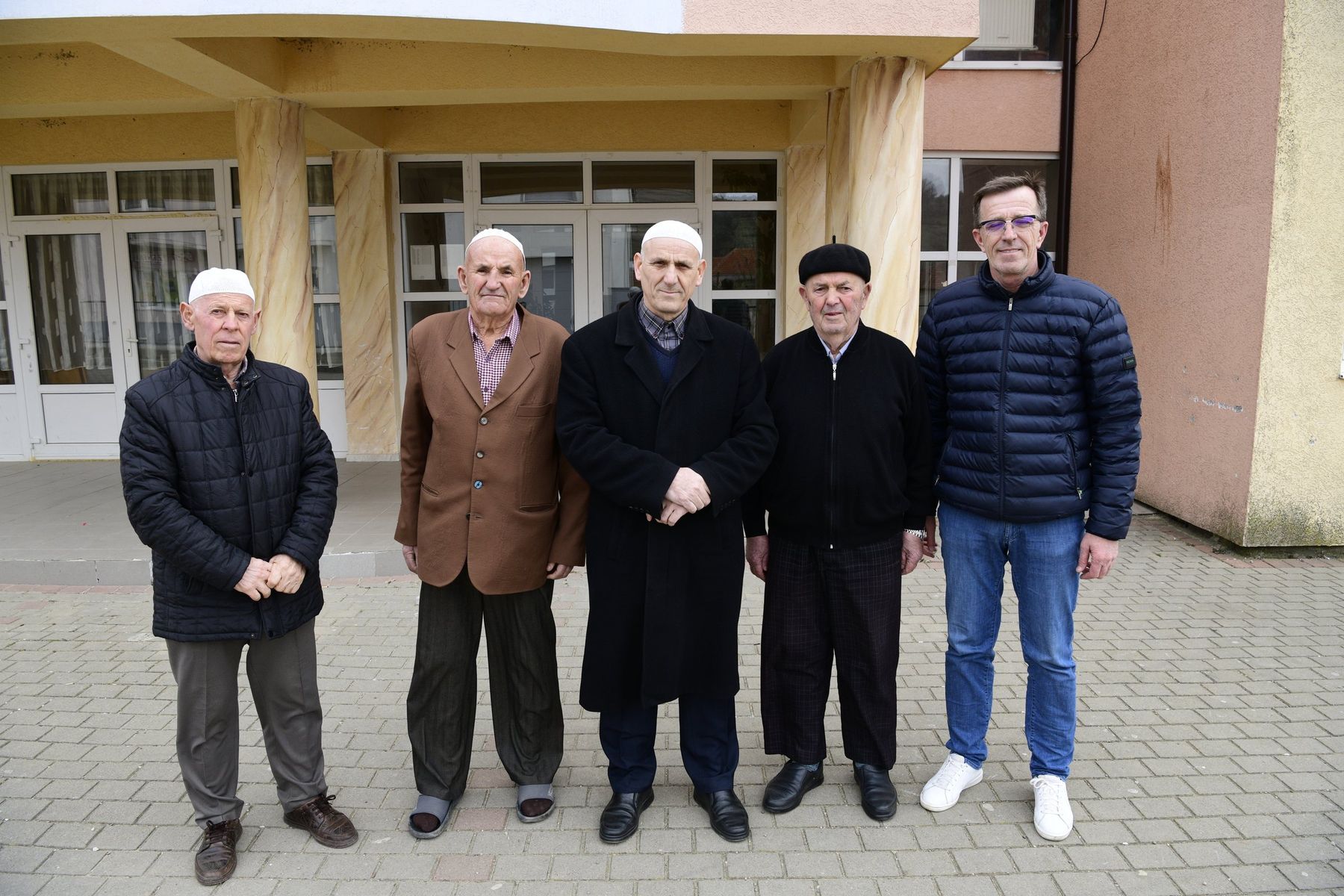 Five men stand in a row in front of a school building