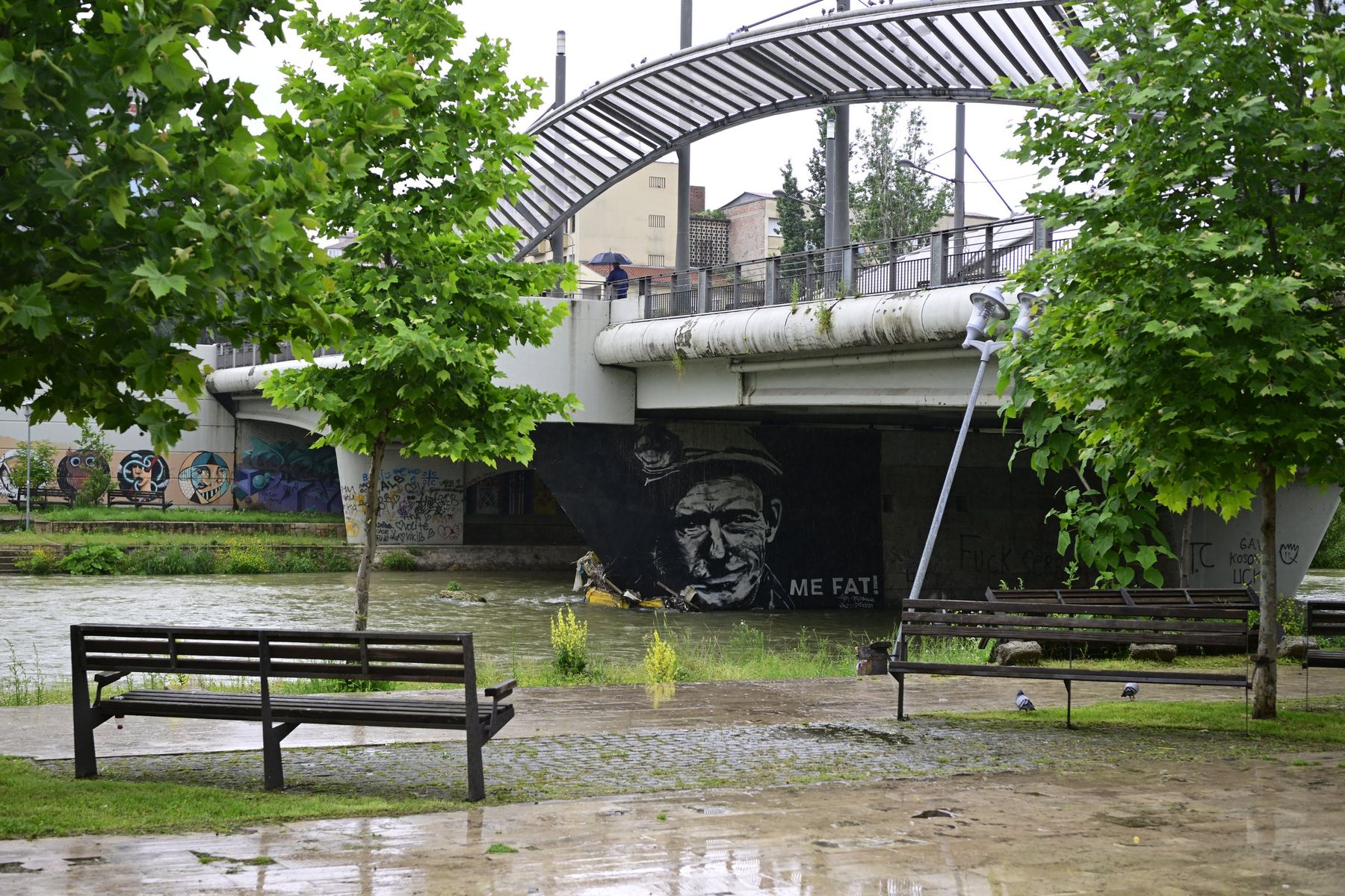 A bridge over a river, with benches and trees on the bank