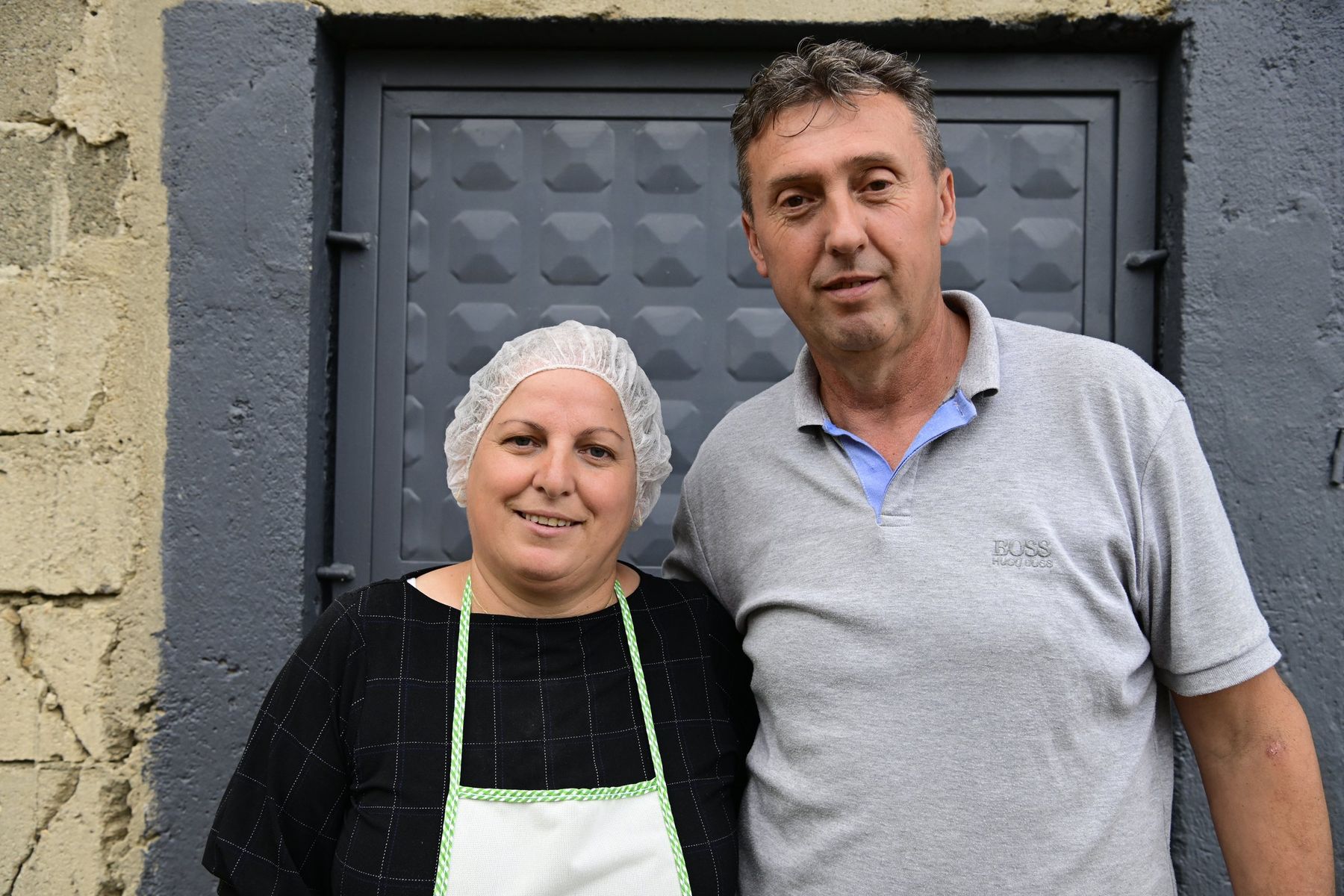 A woman in an apron and a man stand before a metal gate