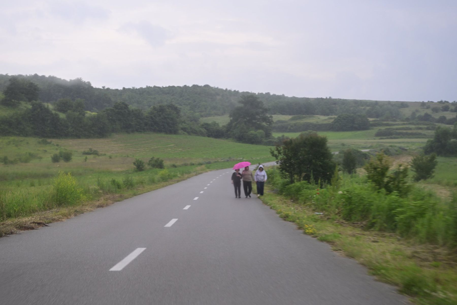 A long road through green hills, a few people walking far away