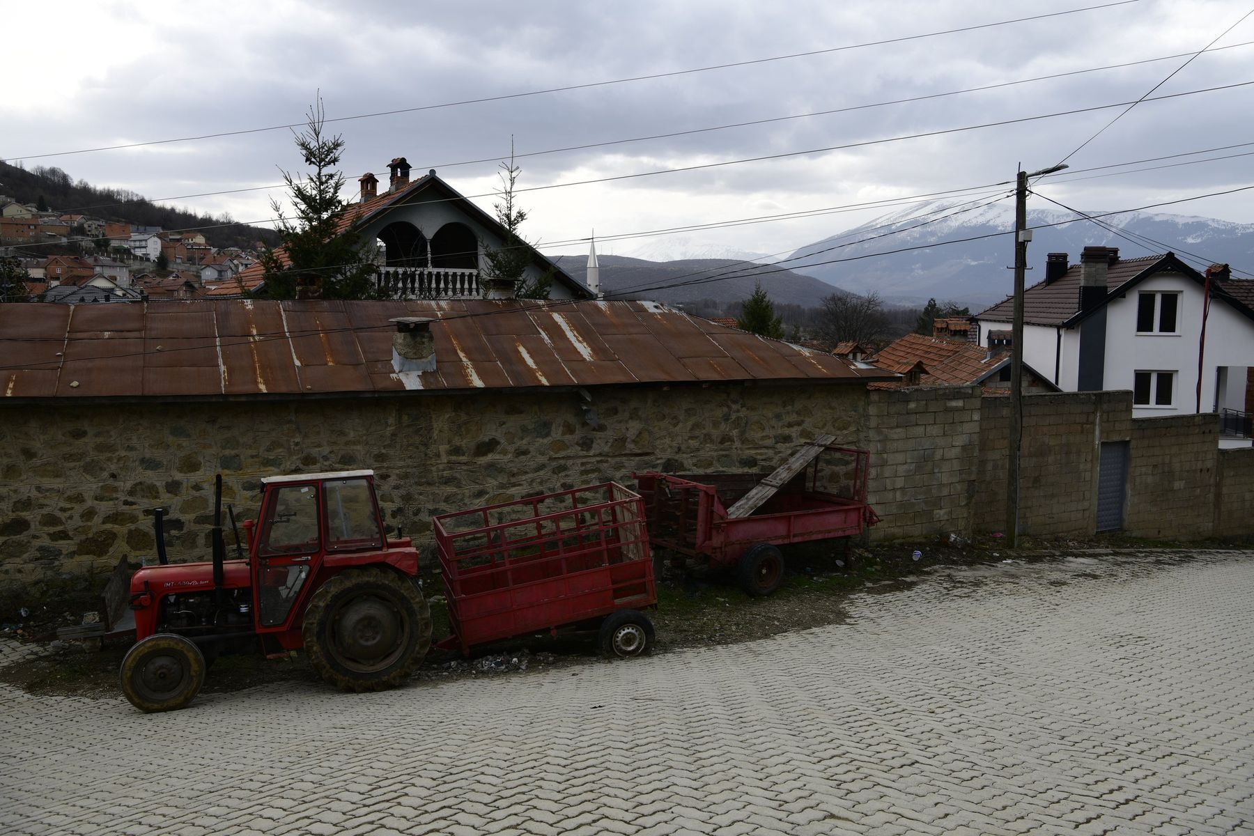 A red tractor and trailer below tiled roofs and snowy mountains