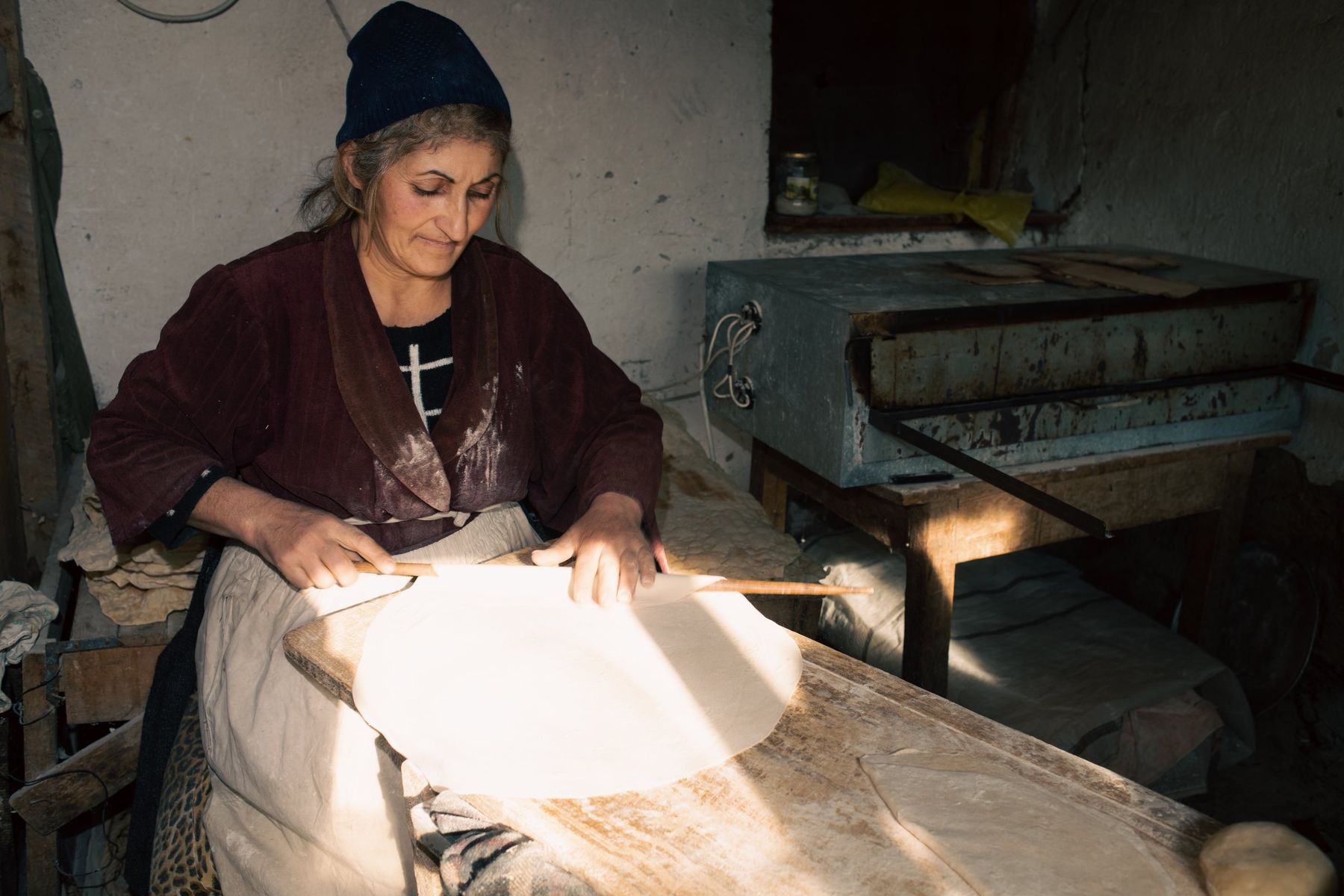 A woman stretches lavash dough by the light of a doorway