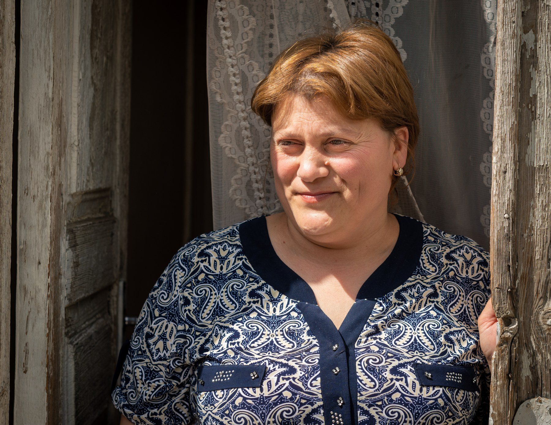 A woman in a patterned blouse leans in a wooden doorway