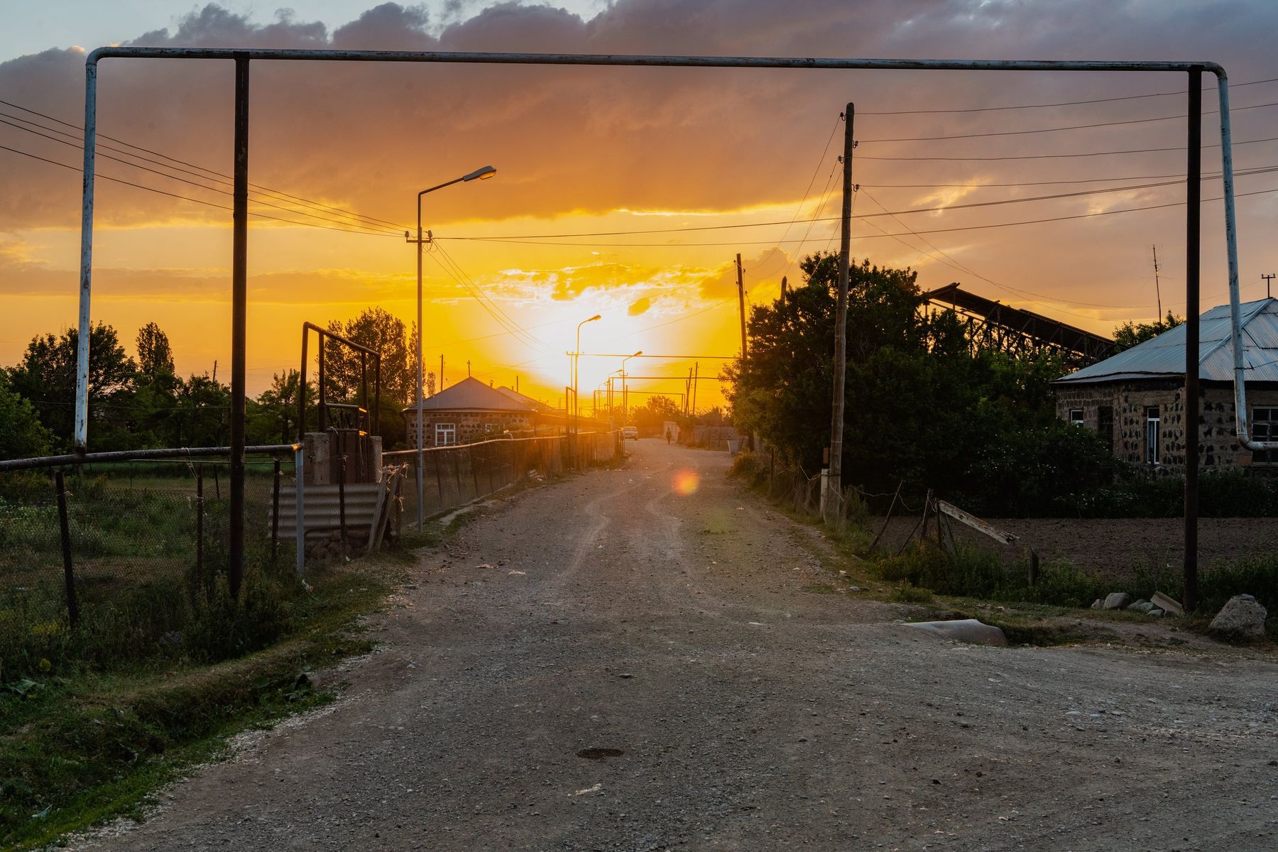 A village road at dusk, the sun setting at the far end