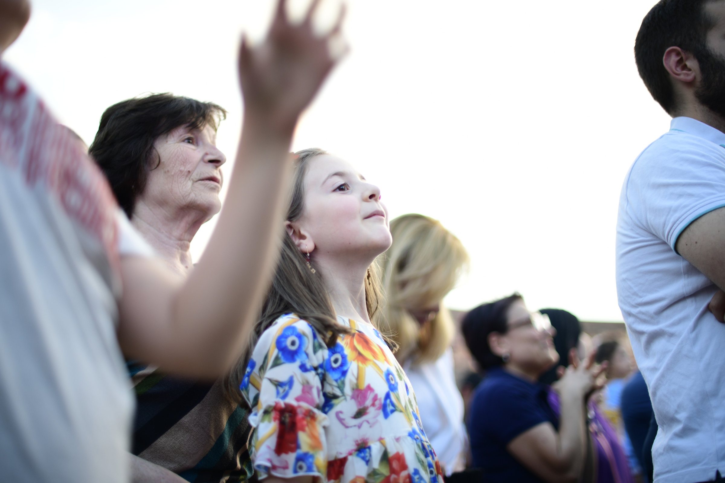A girl in a floral dress looks up beside her grandmother, a hand raised above them
