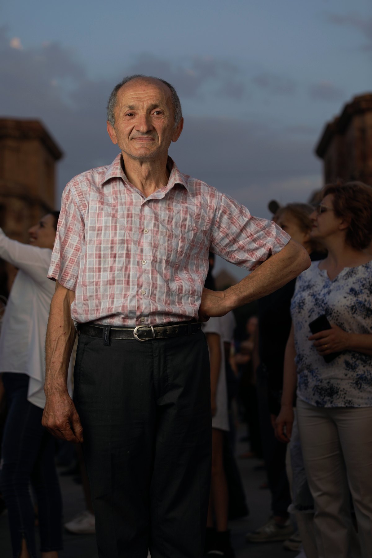 An elderly man in a checked shirt stands in the crowd, hand on hip, before he is given the whiteboard