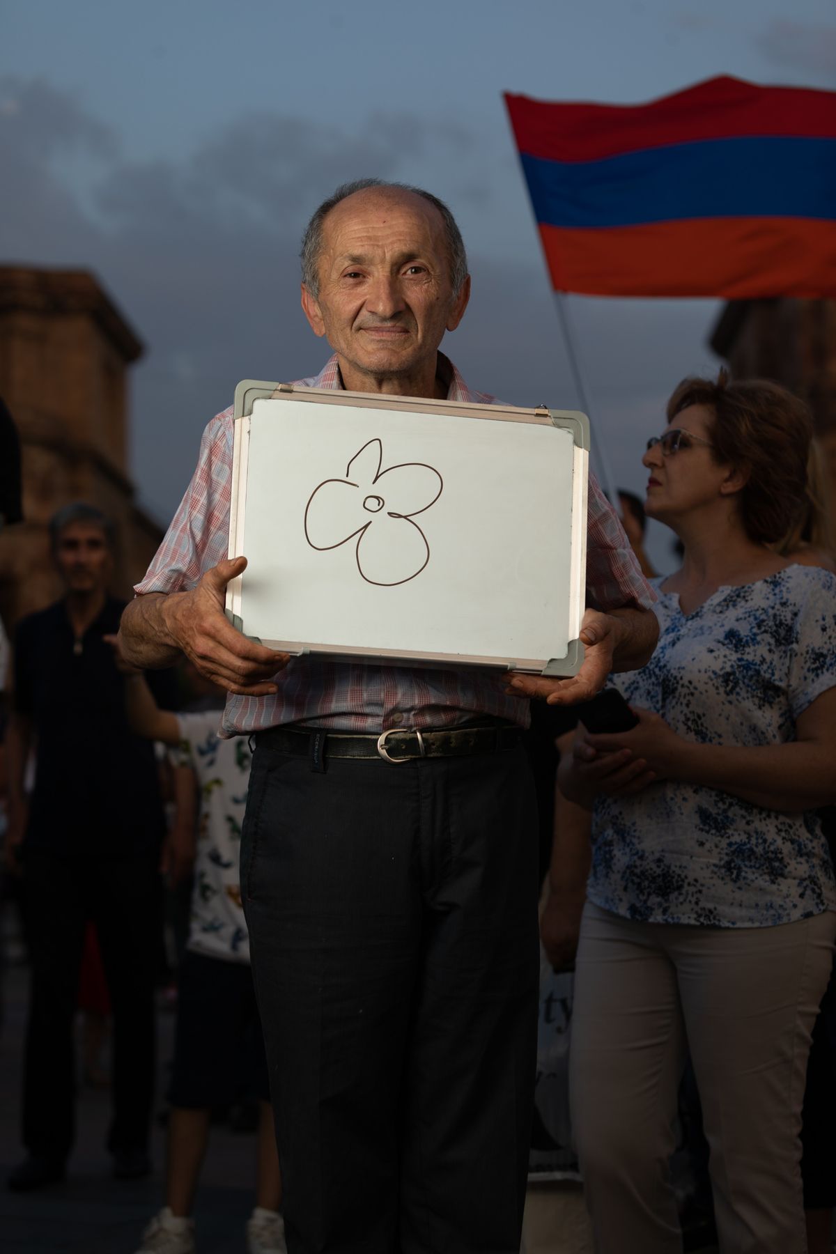 The same man holds up his whiteboard with a drawing of a flower